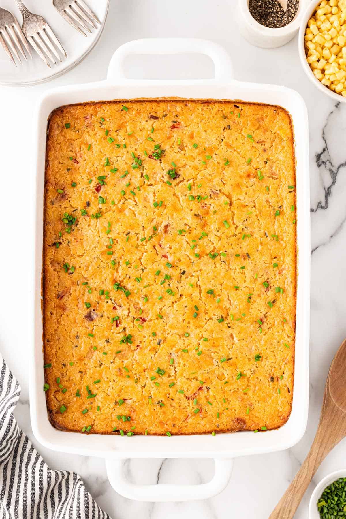 Fully baked cornbread pudding in a white casserole dish, golden brown and topped with chopped chives