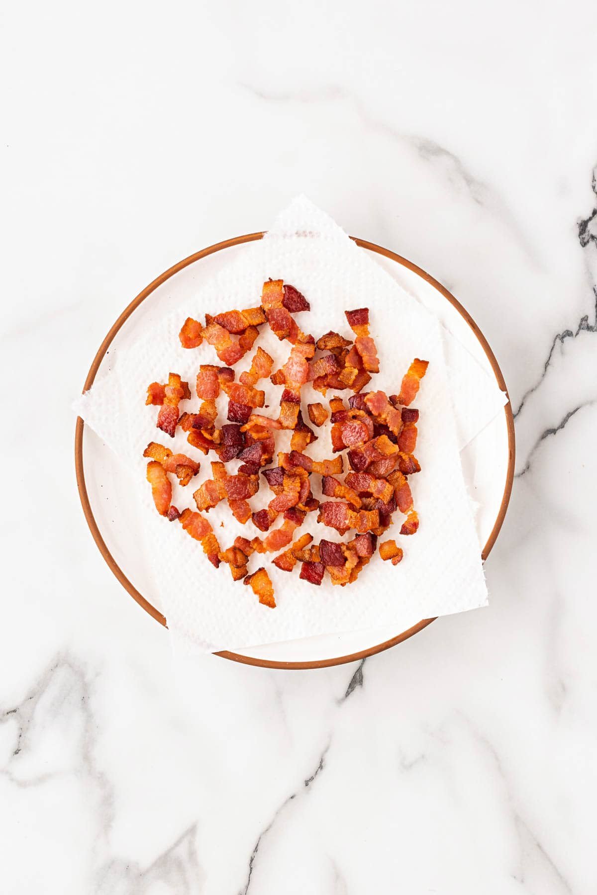 Crispy cooked bacon pieces draining on paper towels in a bowl