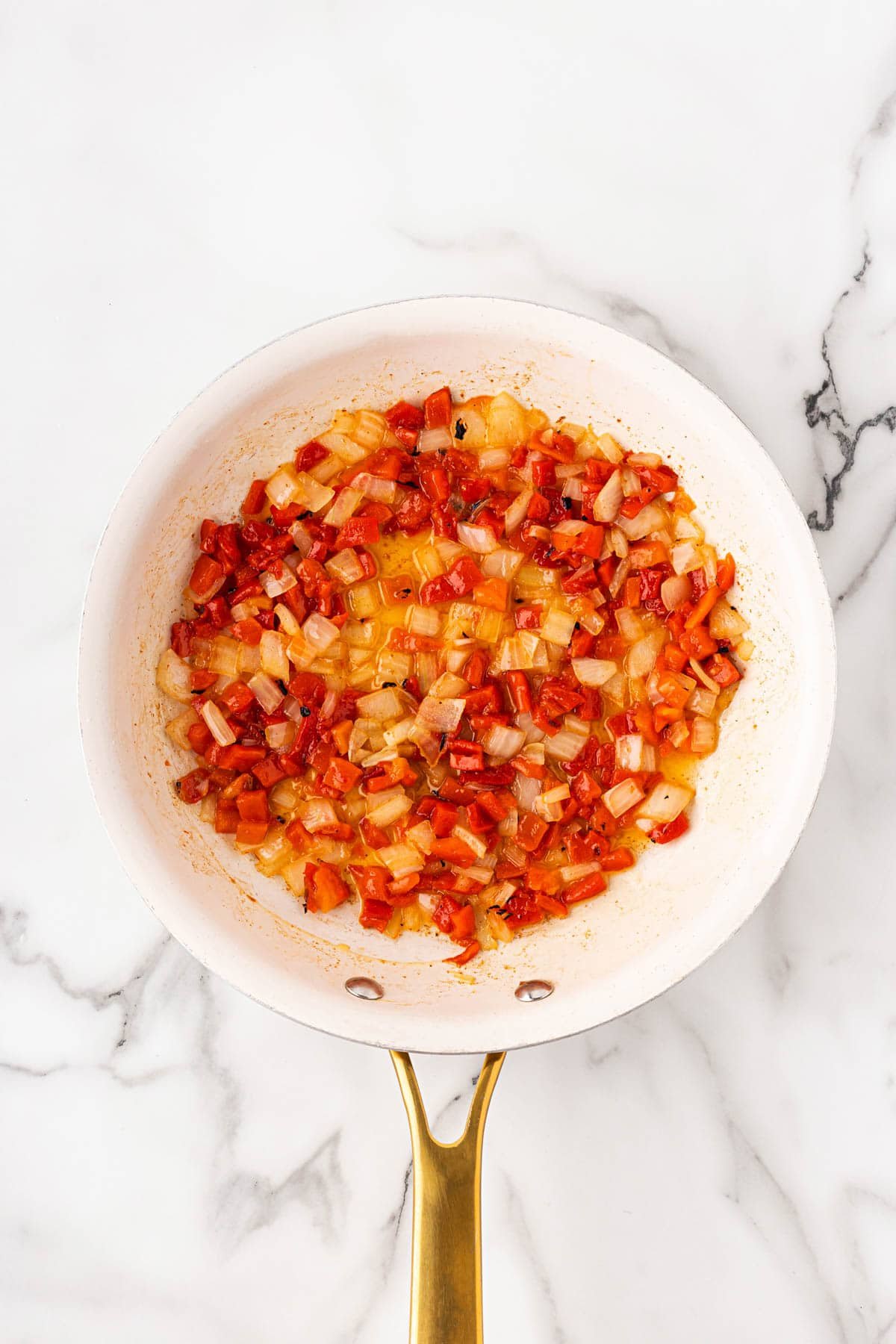 Sautéed diced onions and red bell peppers in a white skillet