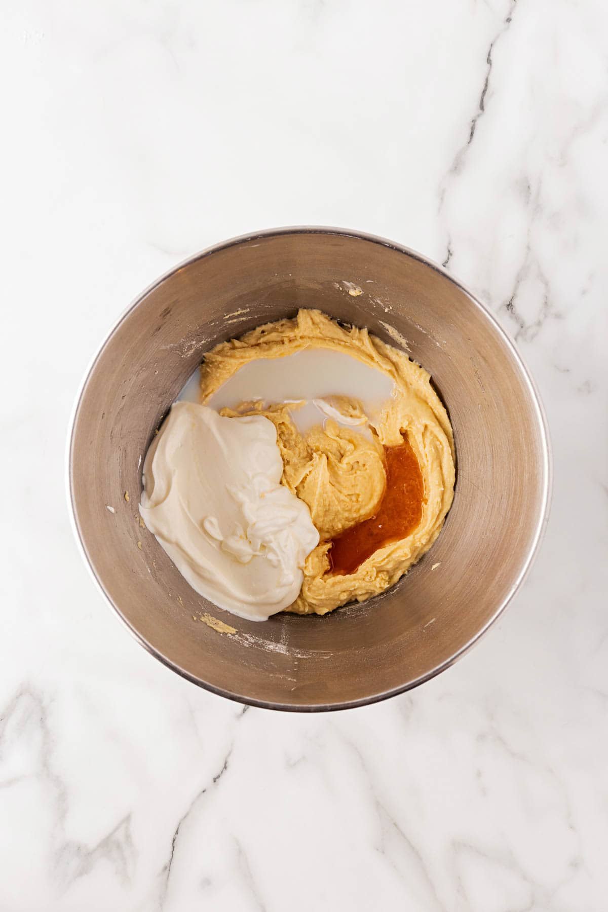 Mixing bowl containing cake batter with sour cream, milk and vanilla added before blending