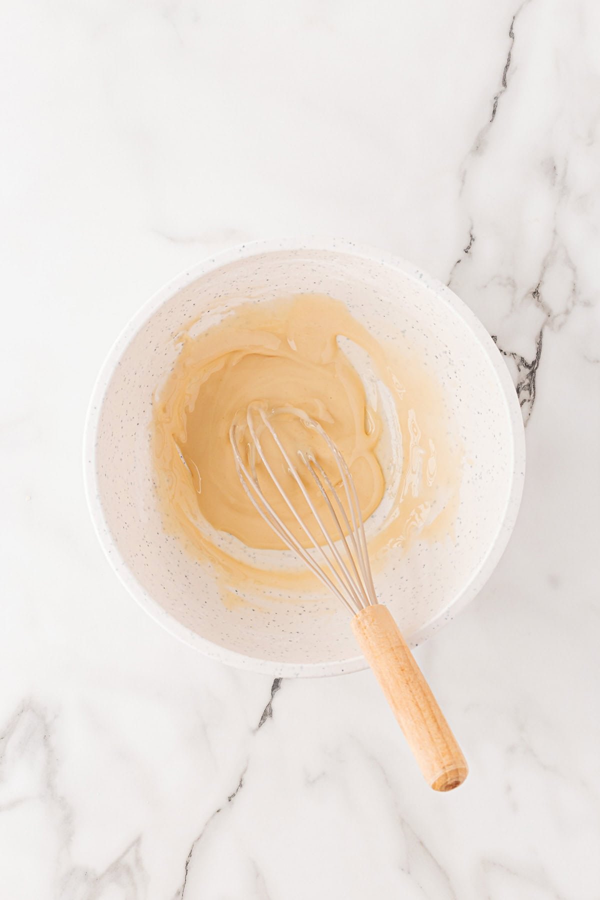 Overhead shot of a bowl containing vanilla honey glaze being whisked on a marble surface