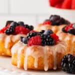 Closeup of glazed mini honey bundt cakes topped generously with assorted fresh berries on a white plate