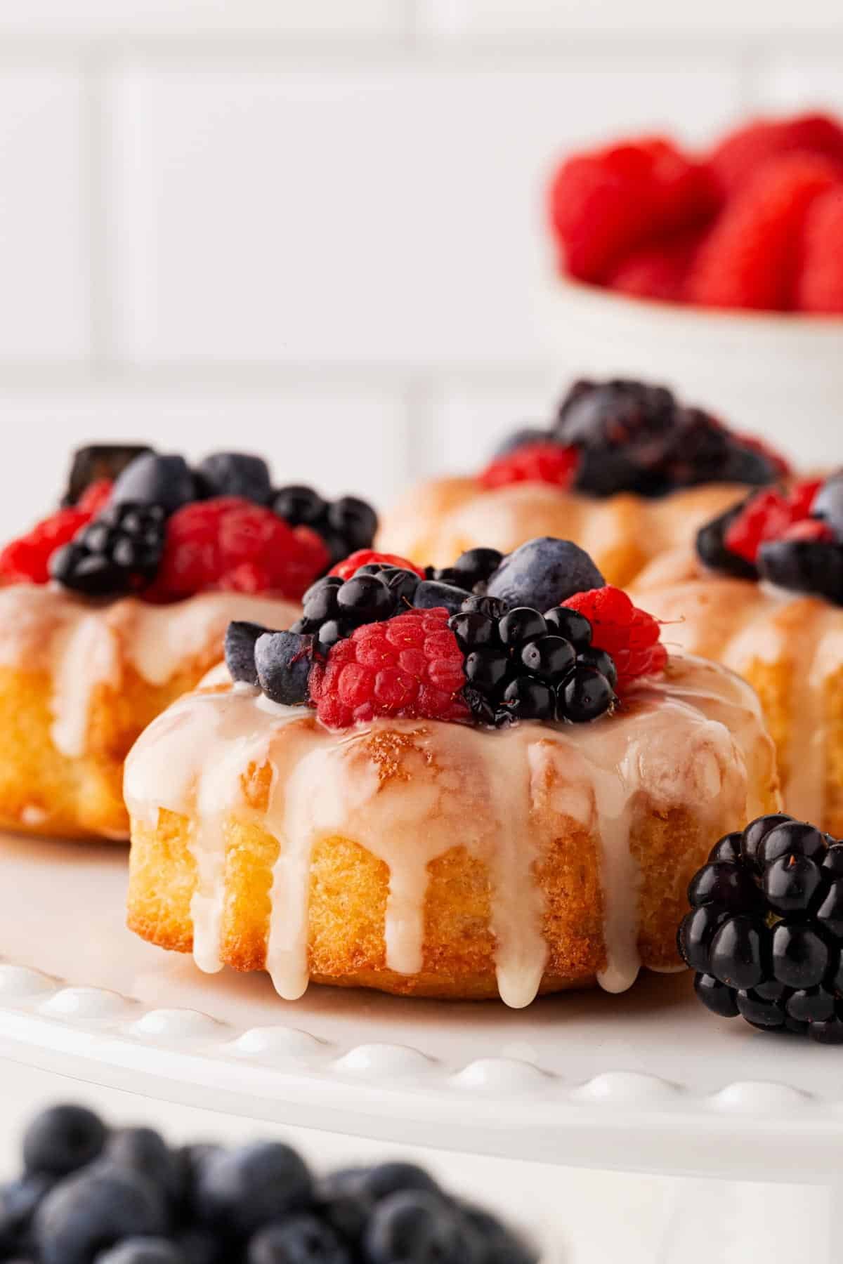 Closeup of glazed mini honey bundt cakes topped generously with assorted fresh berries on a white plate