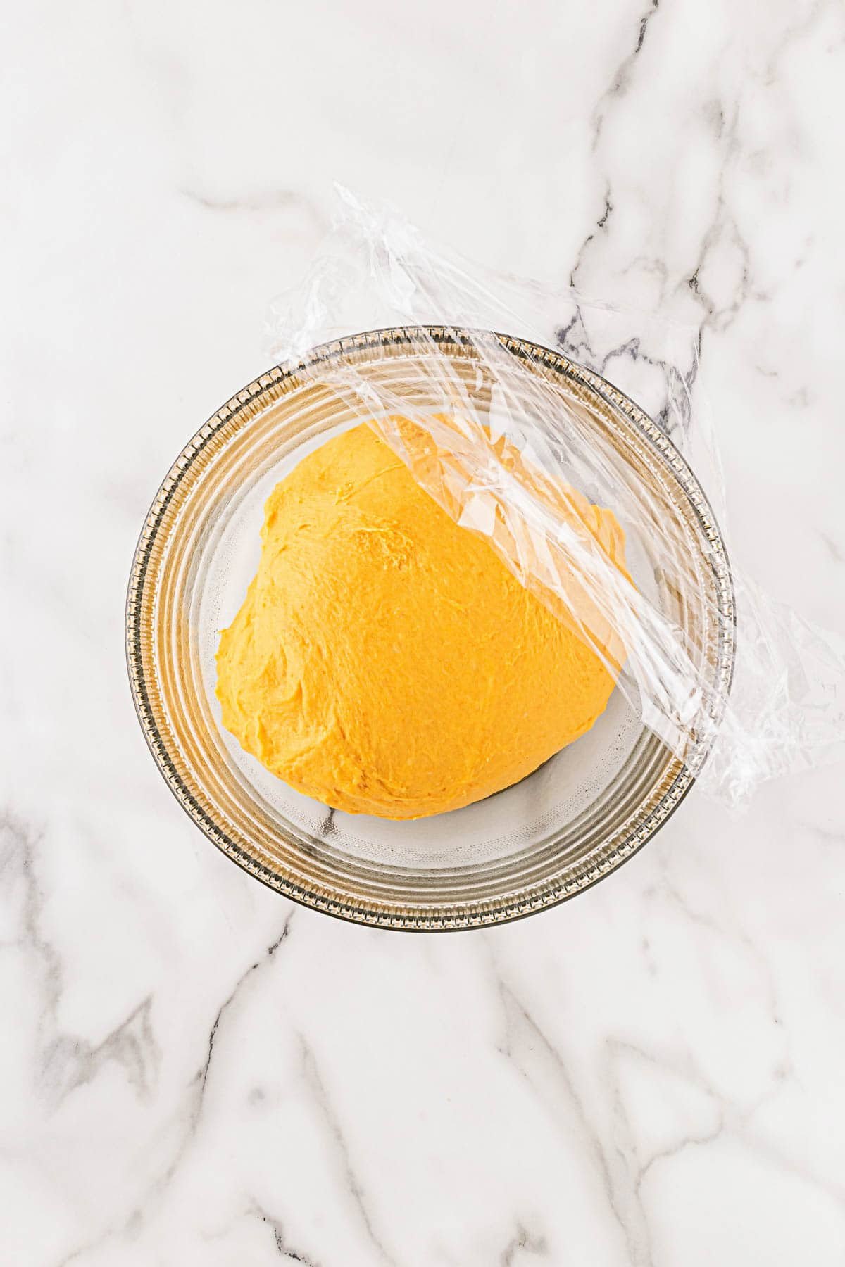 Bowl with smooth pumpkin dough covered in plastic wrap to rise