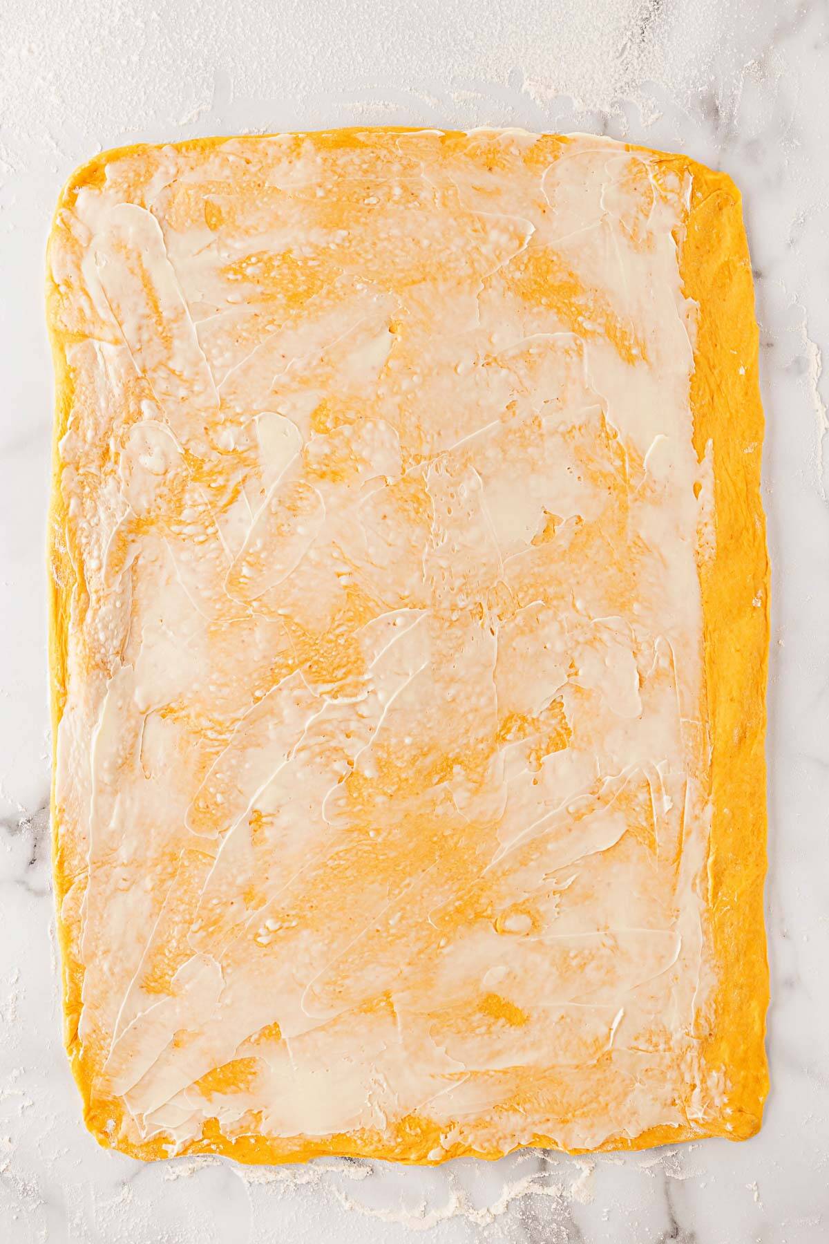 Rolled-out pumpkin dough sheet spread with softened butter