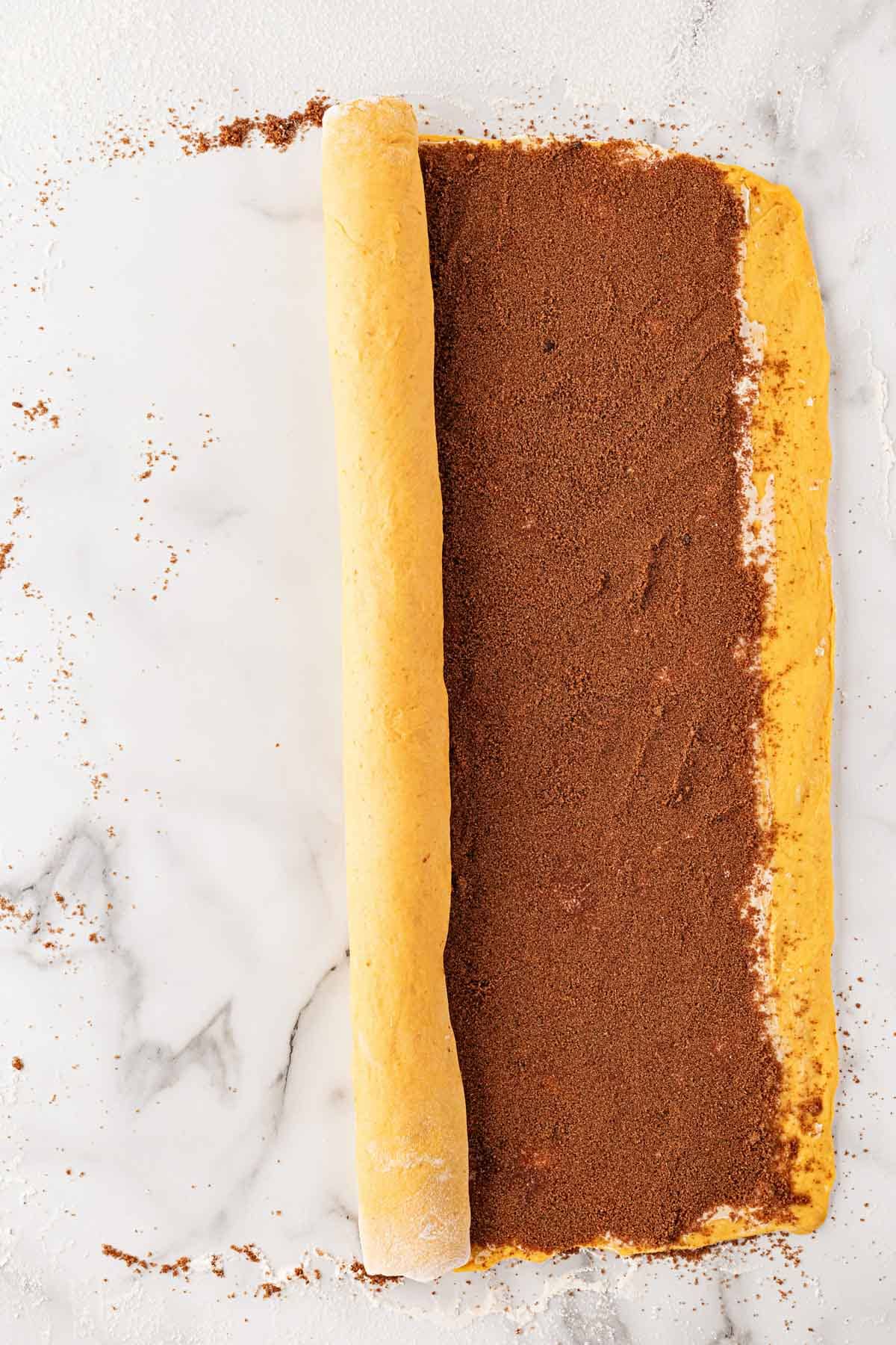 Pumpkin dough being rolled up with a layer of cinnamon sugar filling