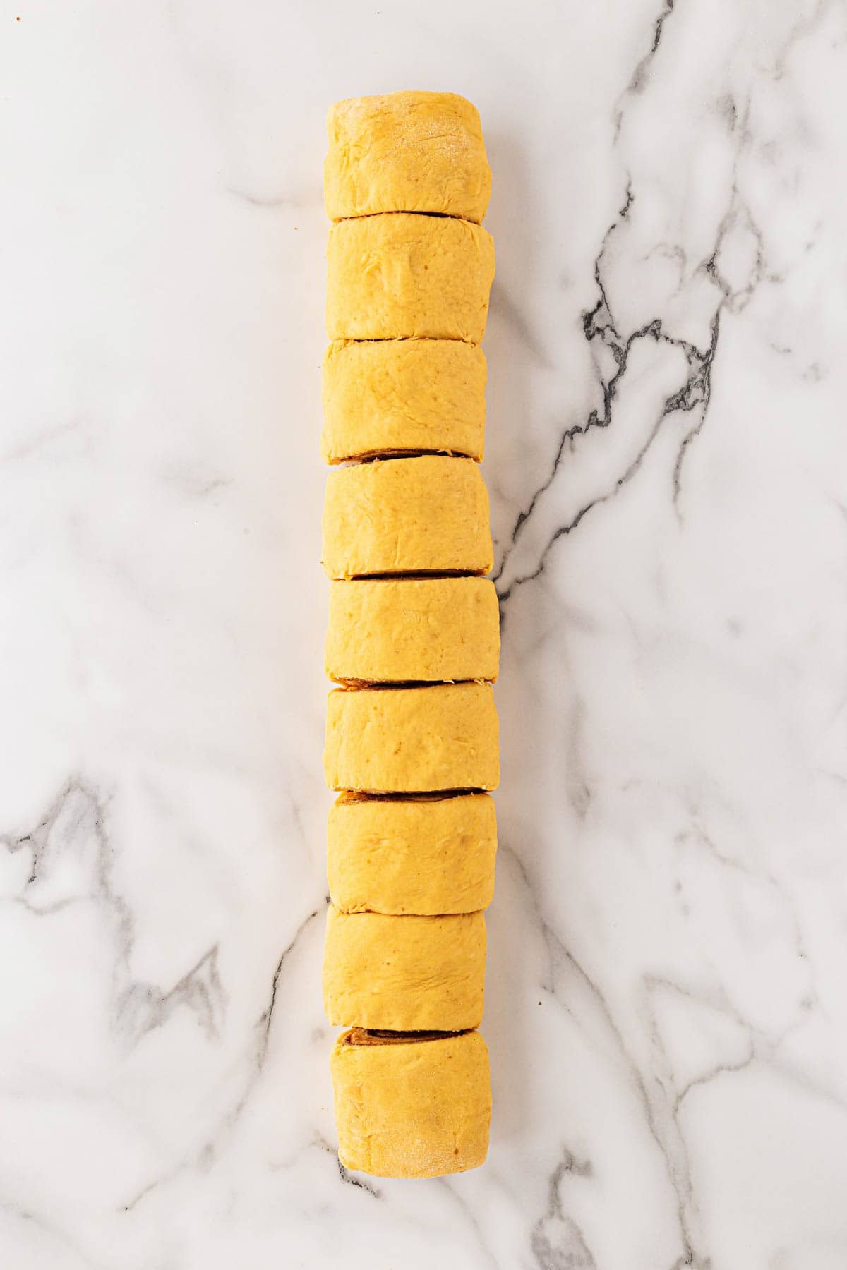 Rolled pumpkin cinnamon roll log sliced into even pieces on a marble surface