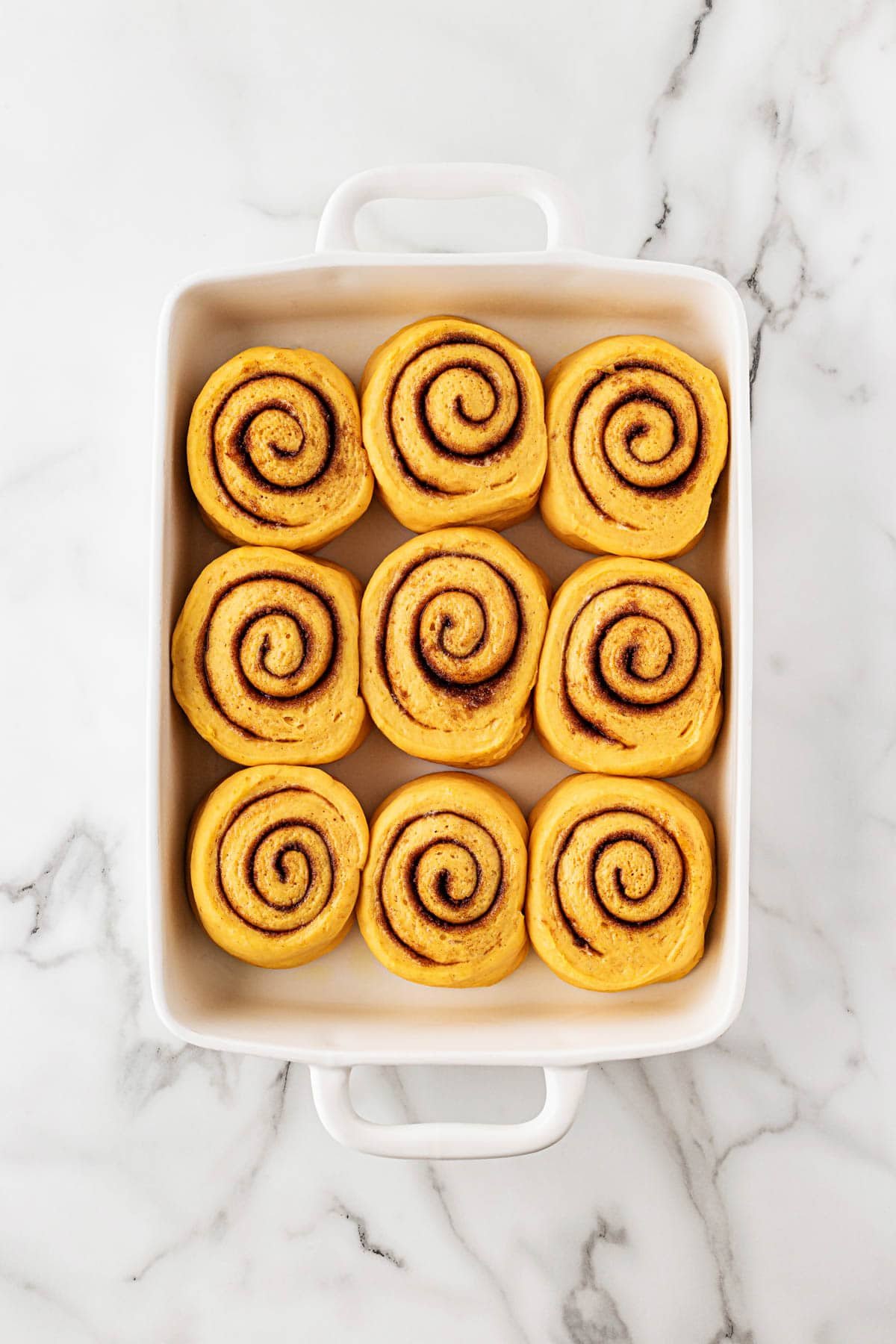 Pumpkin cinnamon rolls arranged in a baking dish before baking