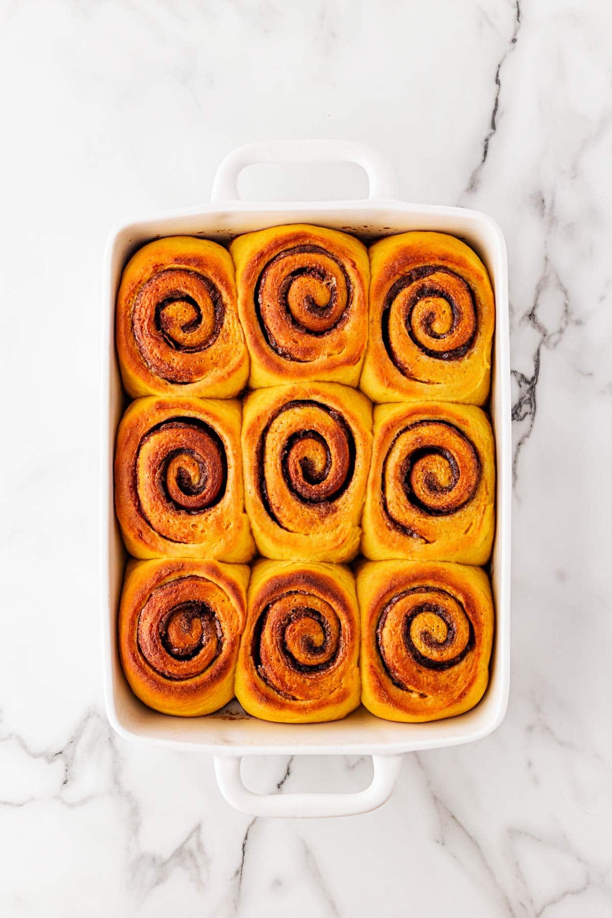 Freshly baked pumpkin cinnamon rolls in a white dish, golden brown