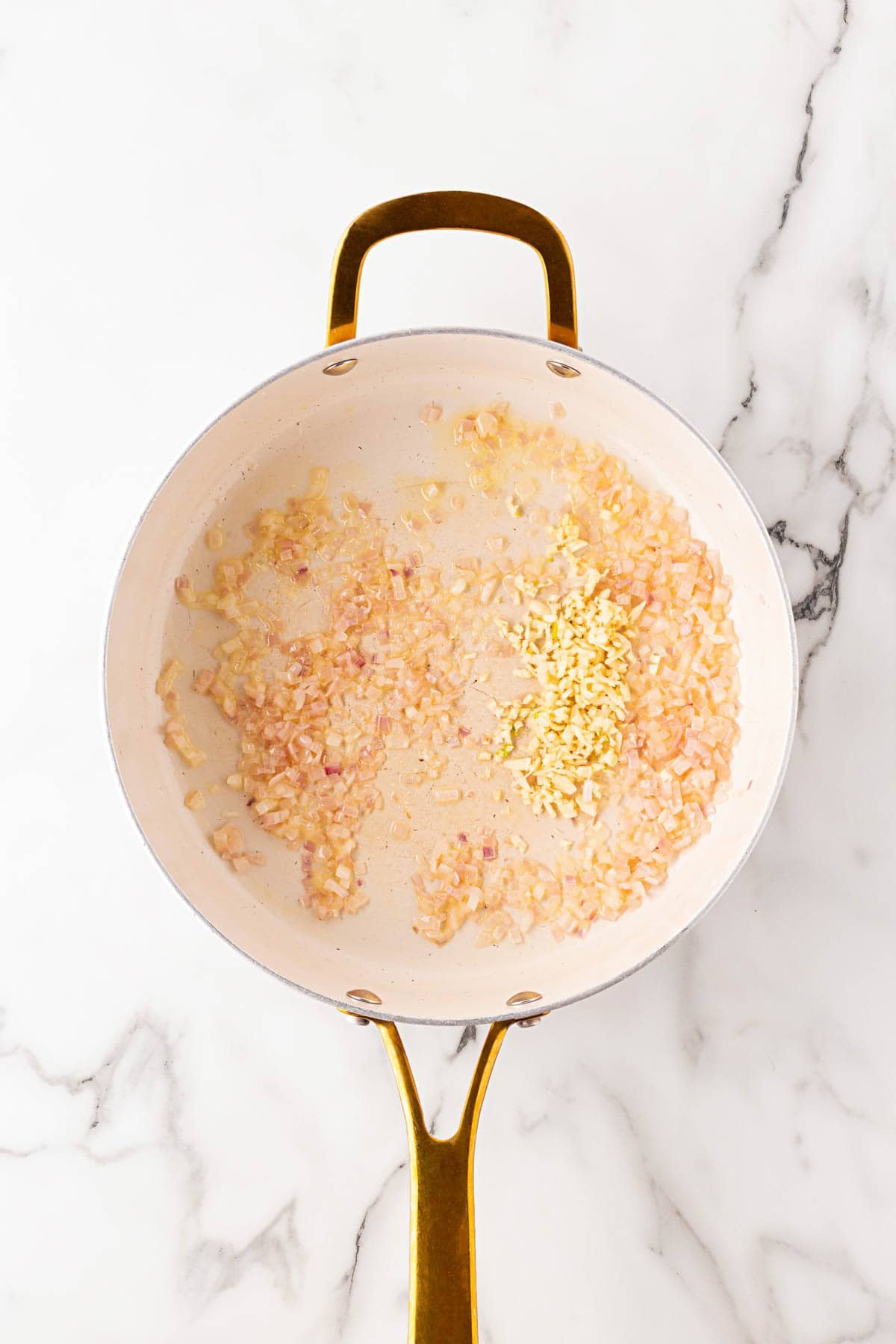 Chopped shallots being sautéed in a skillet with minced garlic added in the center