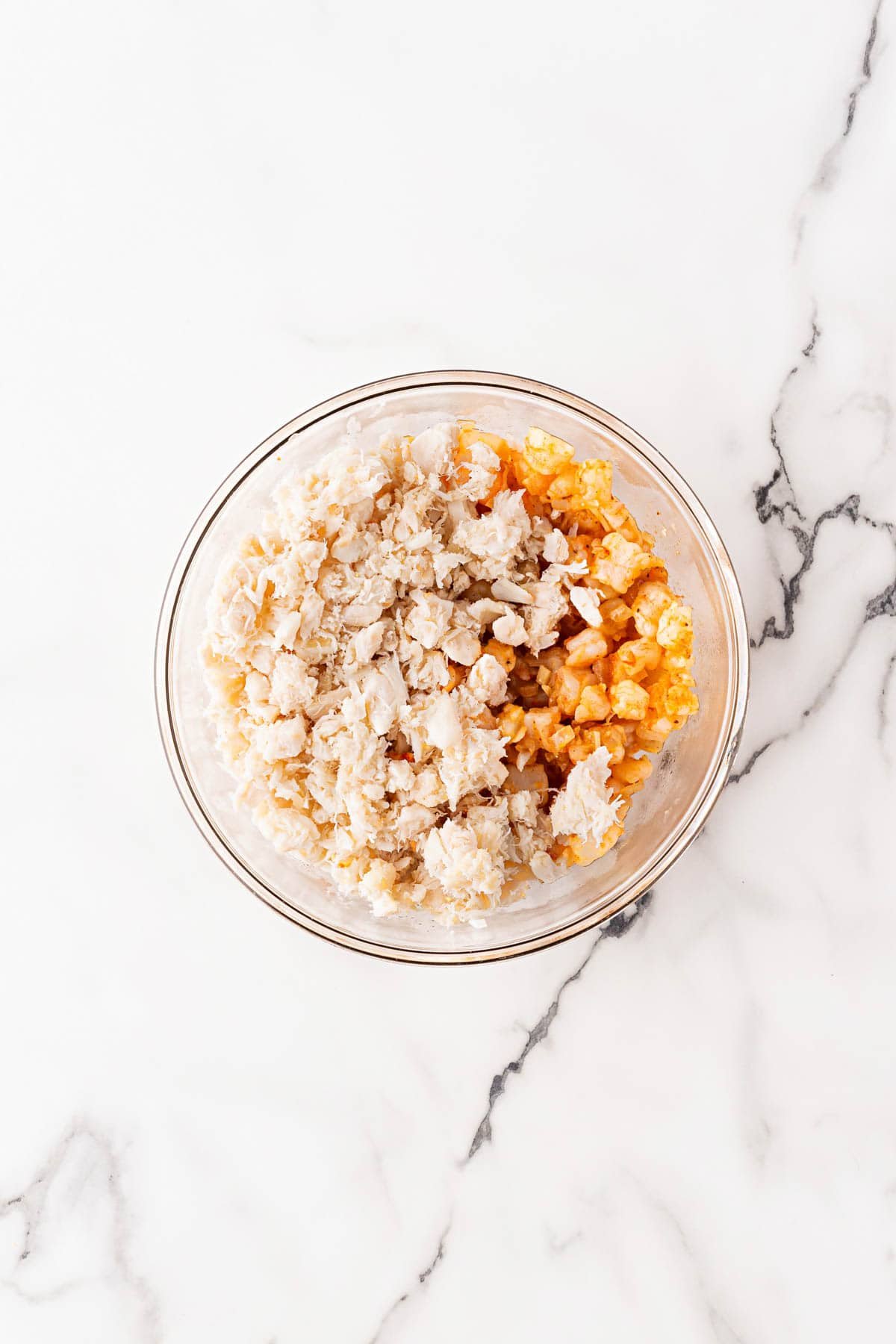 Mixing bowl with cooked shrimp mixture and lump crab meat layered on top before combining