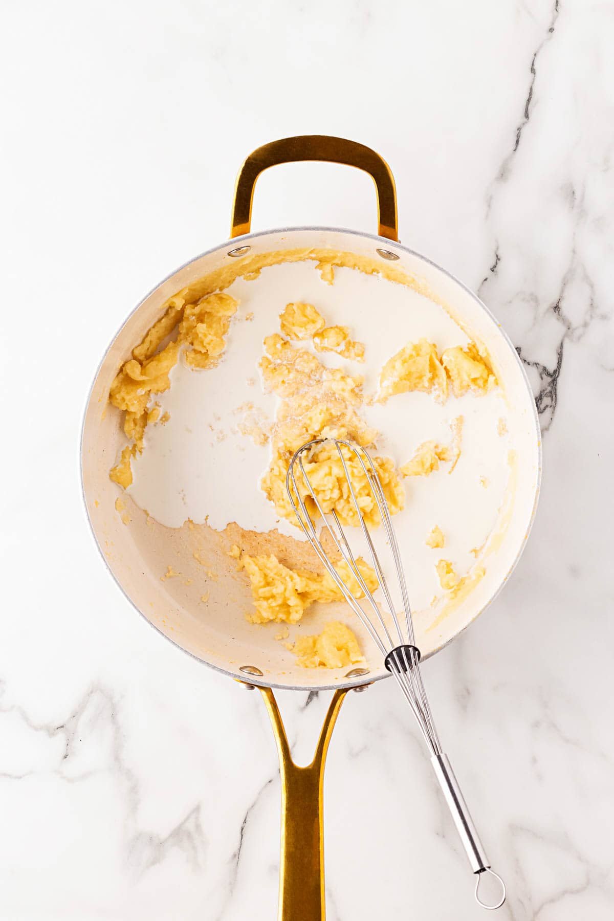 Skillet with a roux mixture being whisked with cream to form a white sauce base