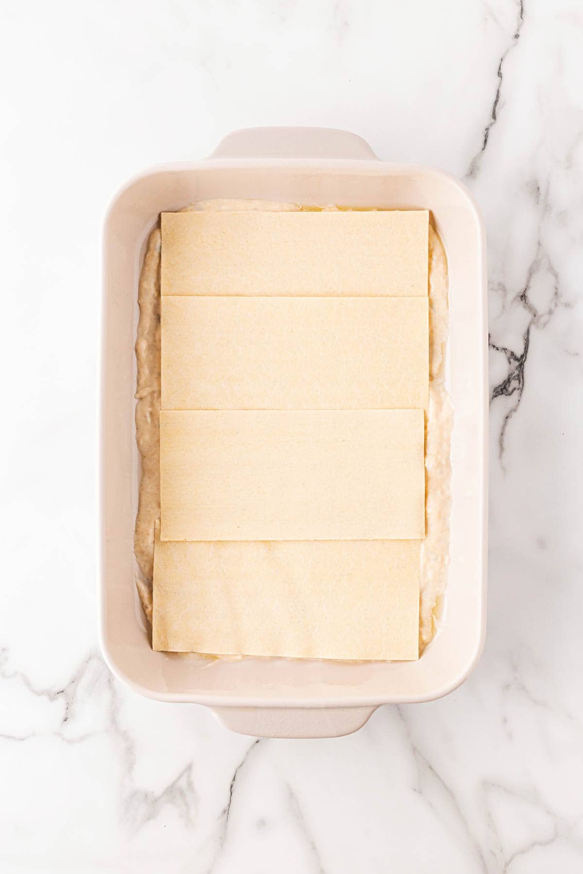 Lasagna noodles neatly arranged in the baking dish over the sauce layer