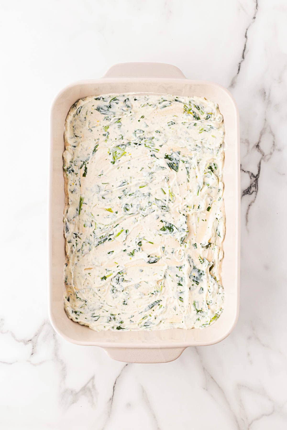 Baking dish with a layer of creamy spinach ricotta filling spread evenly over the noodles