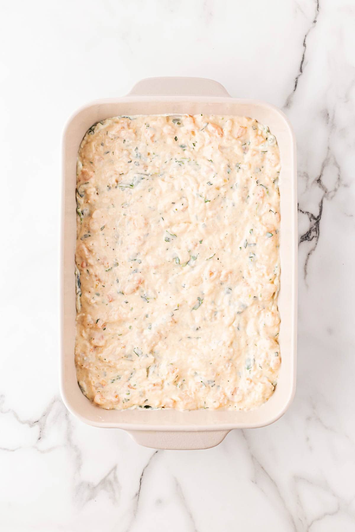Baking dish filled with the final creamy seafood mixture layer spread evenly before topping with cheese
