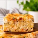 Slice of seafood lasagna lifted from the baking dish, revealing creamy layers of noodles, shrimp, and cheese