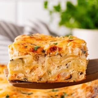 Slice of seafood lasagna lifted from the baking dish, revealing creamy layers of noodles, shrimp, and cheese