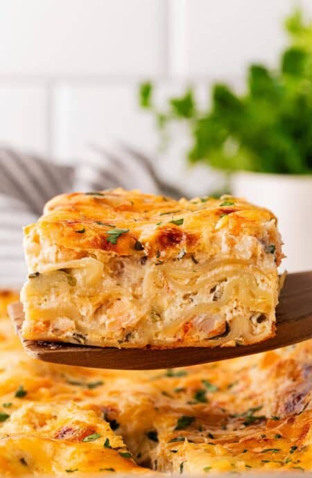 Slice of seafood lasagna lifted from the baking dish, revealing creamy layers of noodles, shrimp, and cheese
