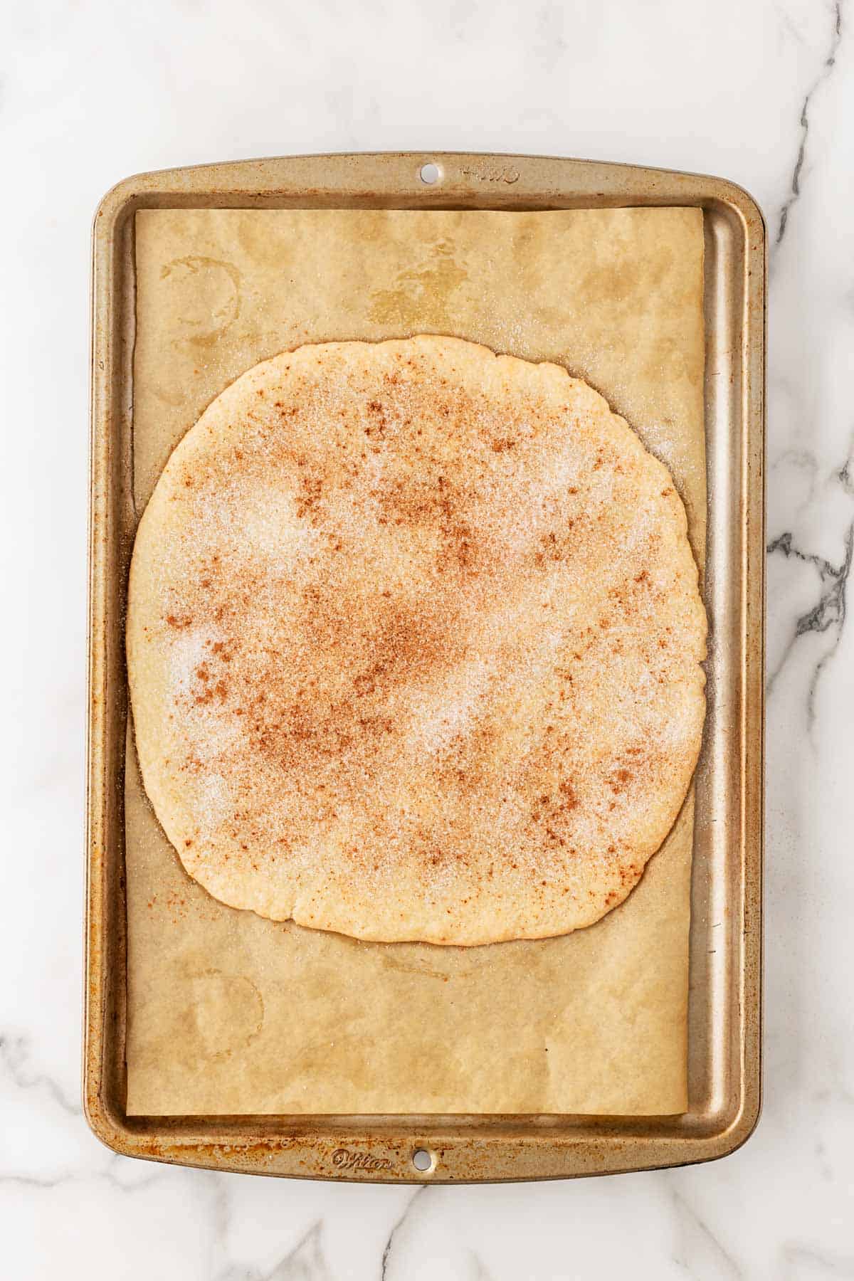 Rolled-out pie dough round sprinkled with sugar and cinnamon on a parchment-lined baking sheet before baking