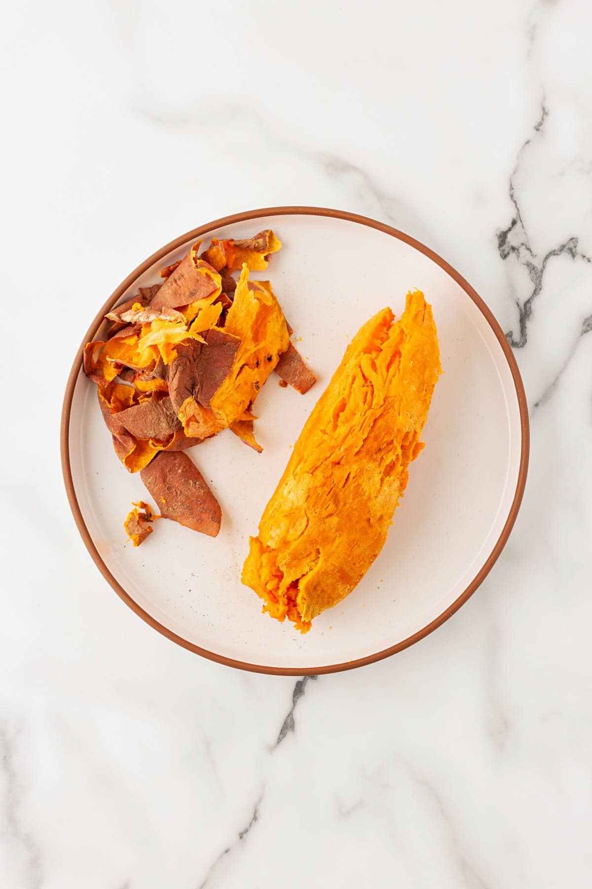 Peeled baked sweet potato on a plate beside the removed skins