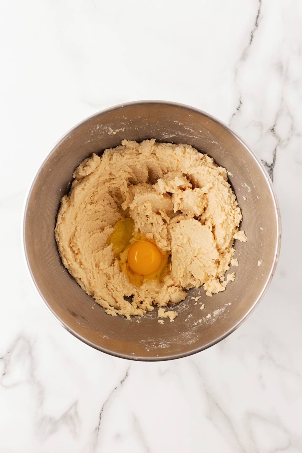 Creamed butter and sugar mixture in a bowl with an egg added on top before mixing