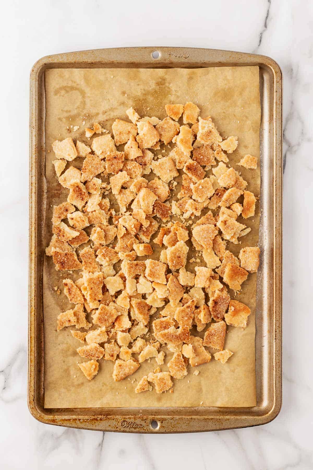 Baked cinnamon sugar dough broken into bite-sized chunks on a parchment-lined baking sheet
