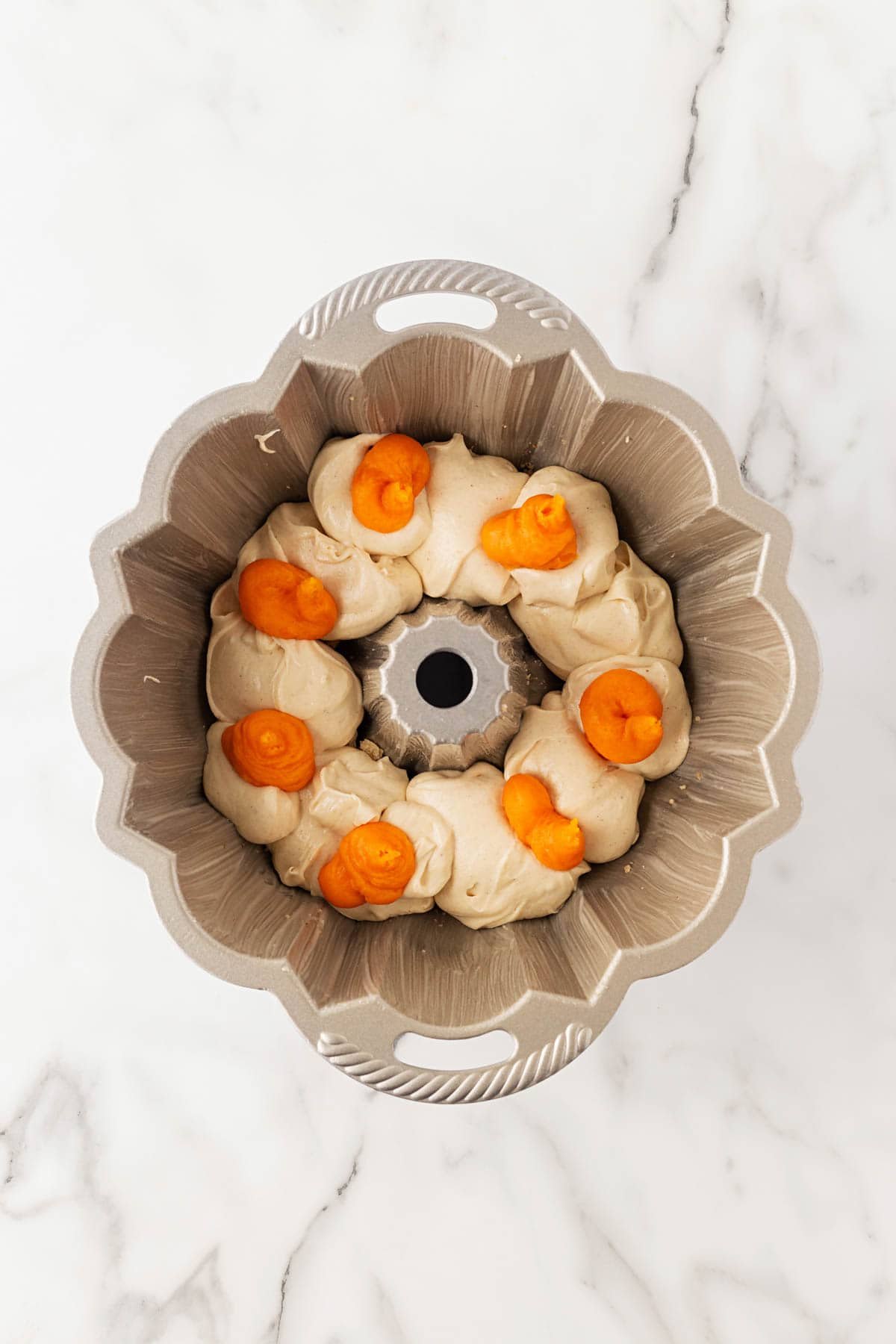 Bundt pan filled with alternating scoops of cake batter and sweet potato mixture