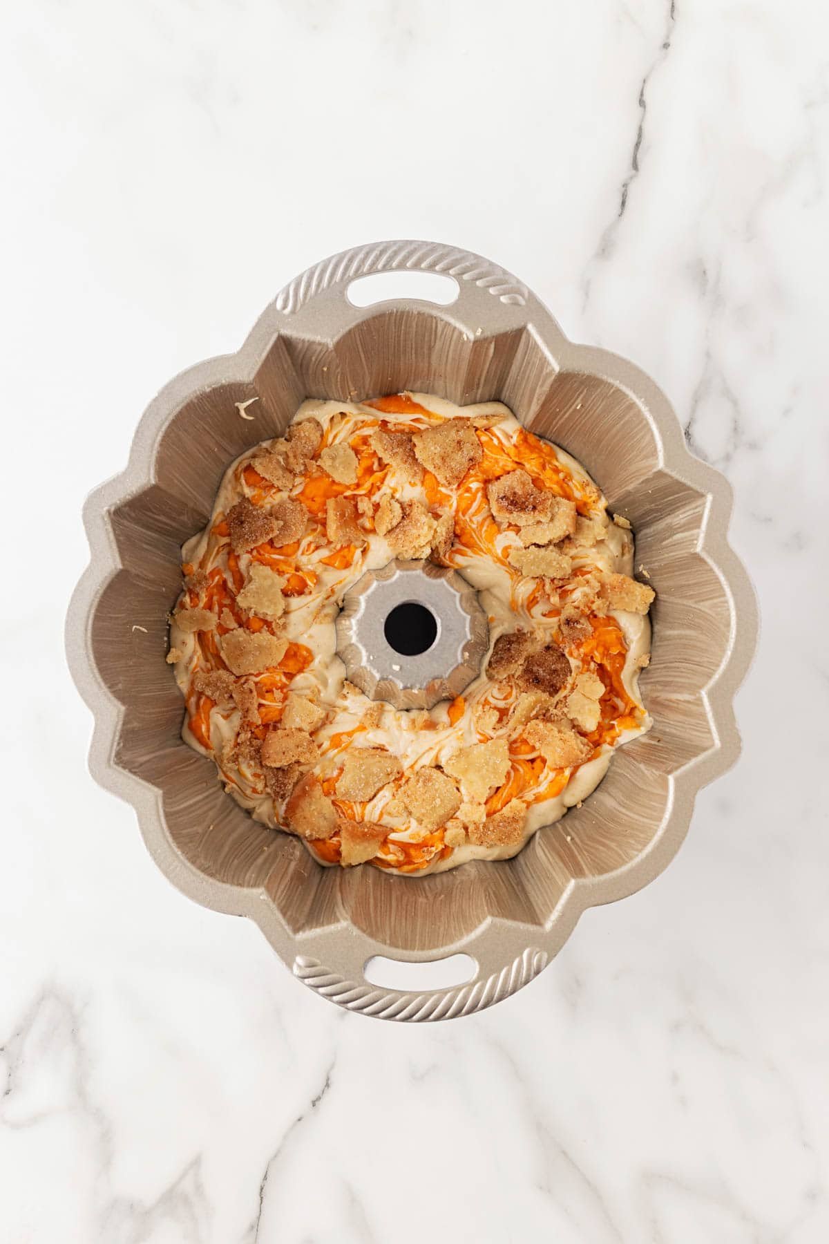 Bundt pan showing swirled batter with sweet potato and dough crumble pieces layered together