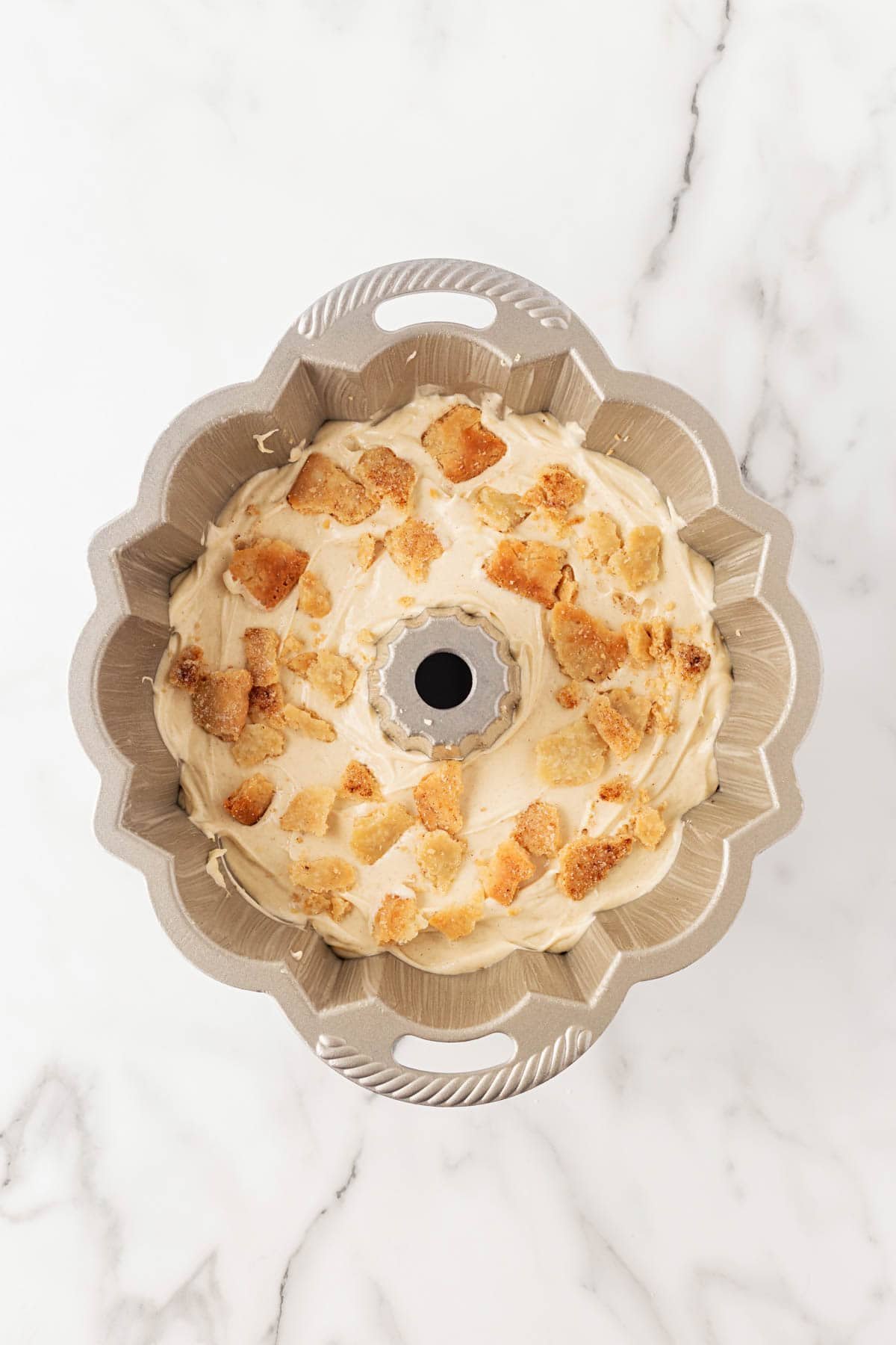 Bundt pan filled halfway with cake batter topped with cinnamon sugar pie crust crumbles