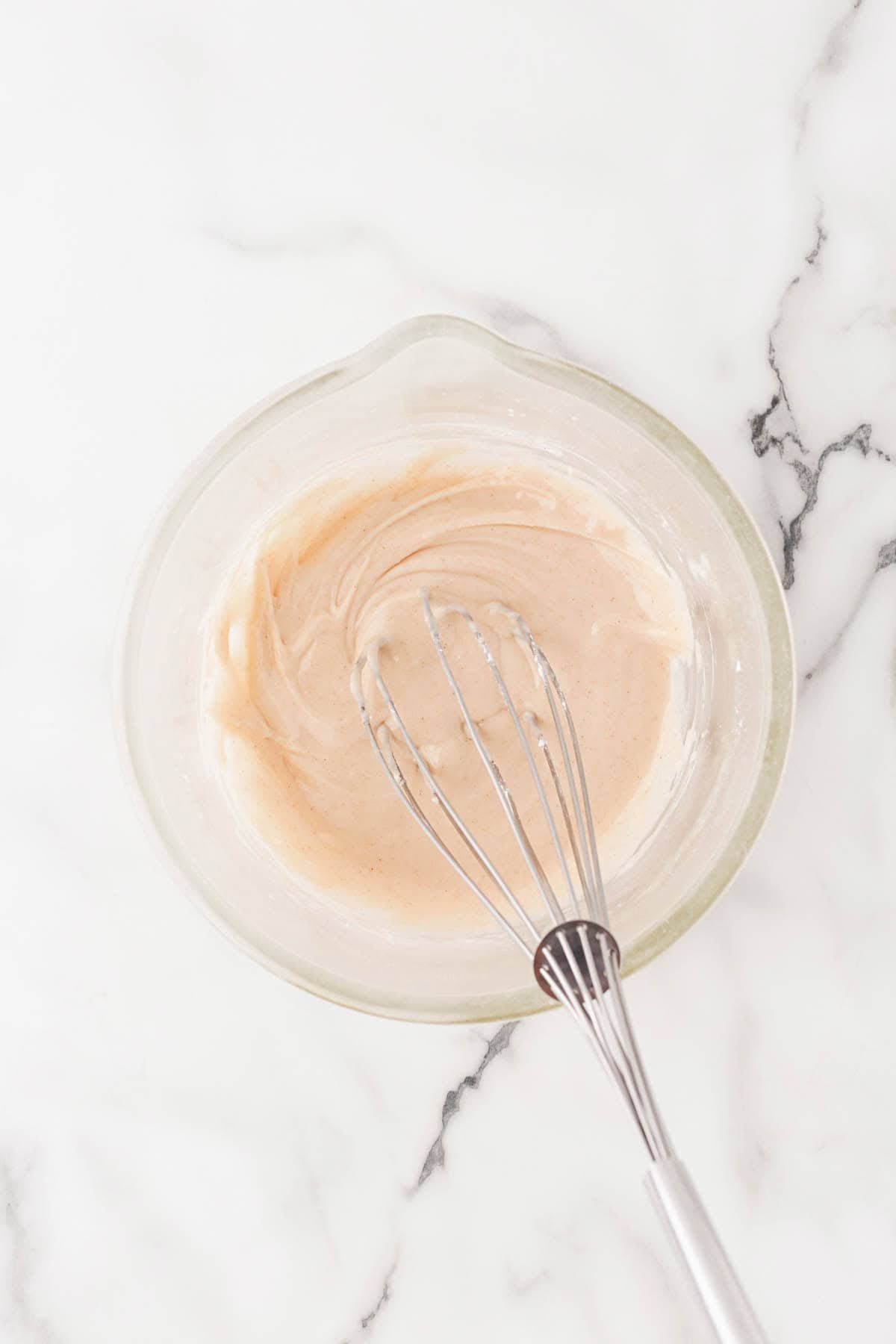 Bowl of cinnamon glaze with a whisk resting inside on a marble surface