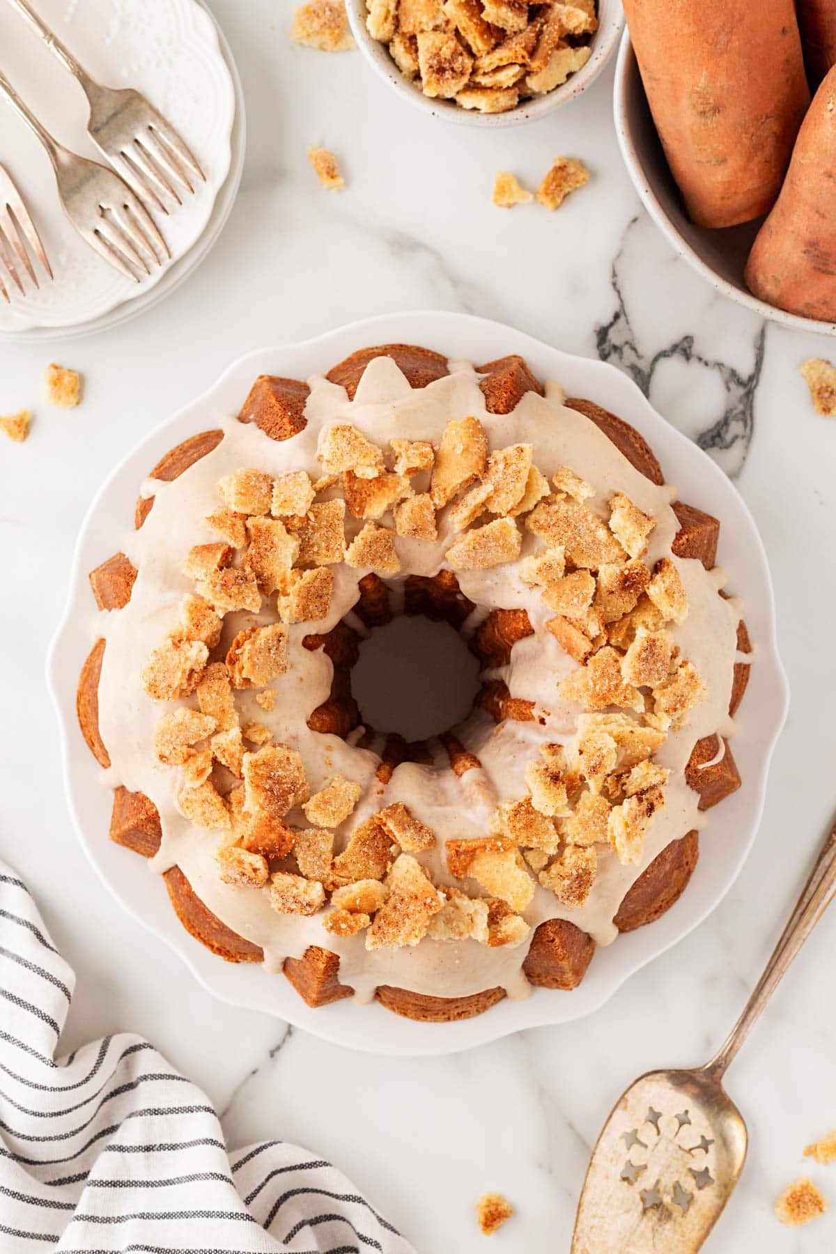 Overhead shot of a sweet potato pie pound cake displayed on a white platter, surrounded by dessert forks, sweet potato, and  a striped napkin