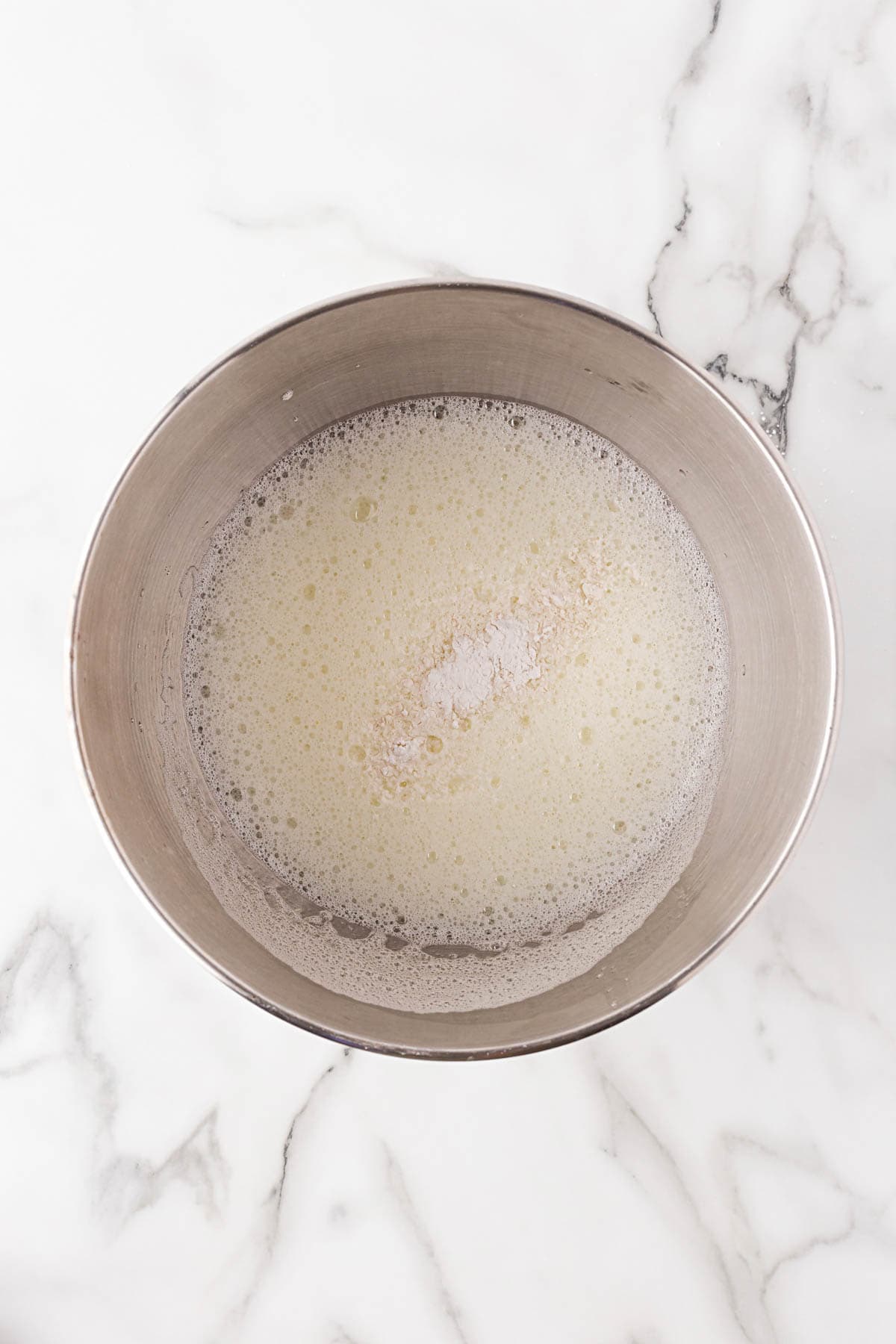 Egg whites in a mixing bowl starting to foam as they're whipped, with cream of tartar added in