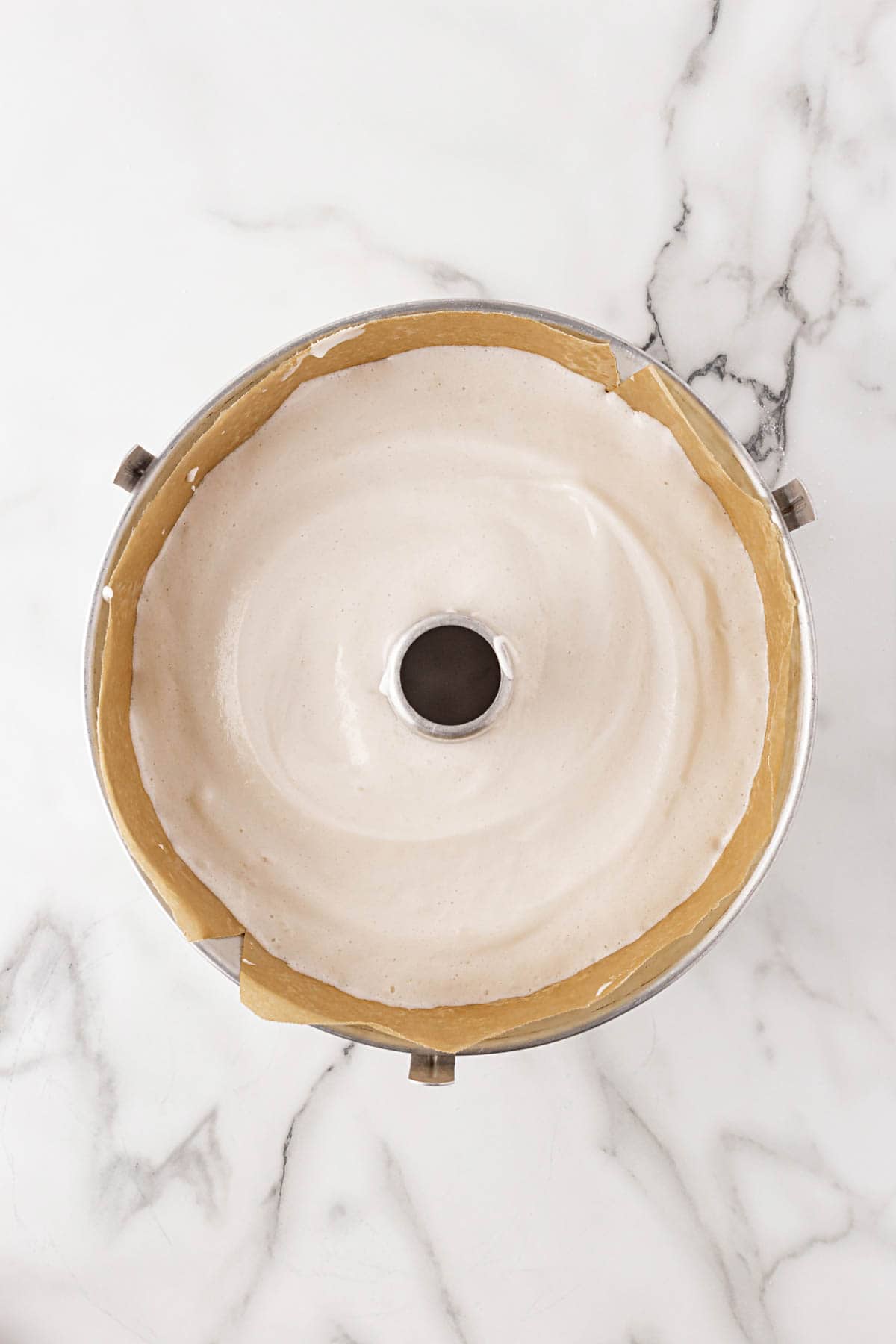 Angel food cake batter evenly poured into a lined tube pan, ready to bake