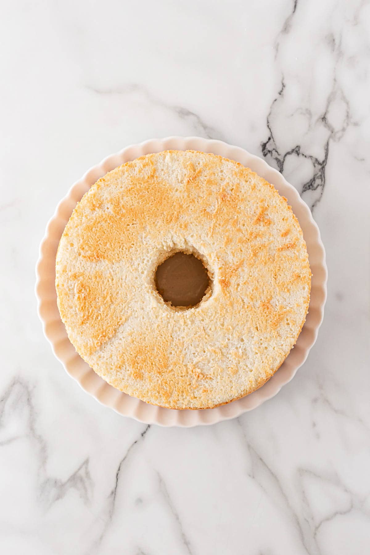 Overhead shot of a plain baked angel food cake placed on a scalloped plate