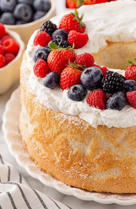 Closeup of a frosted angel food cake topped with fresh strawberries, raspberries, blueberries, and blackberries