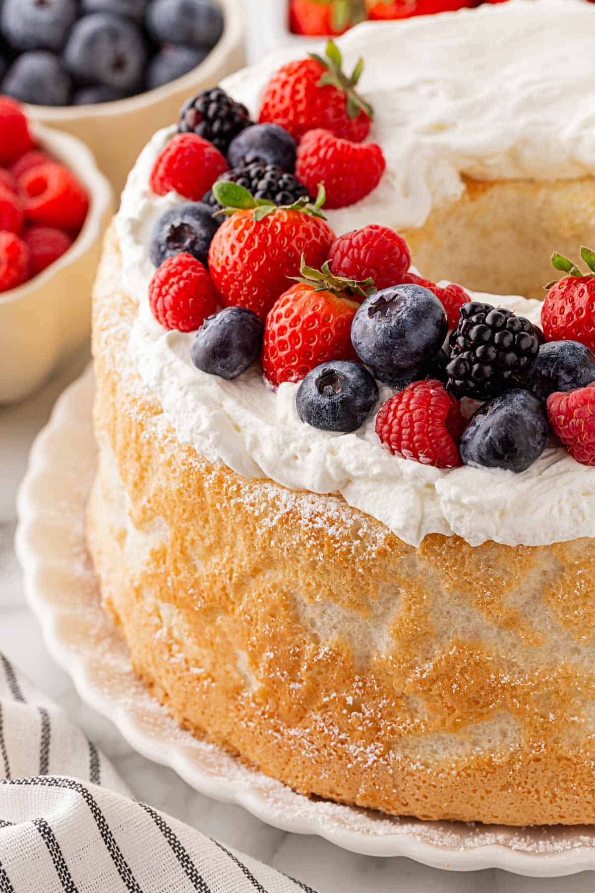 Closeup of a frosted angel food cake topped with fresh strawberries, raspberries, blueberries, and blackberries
