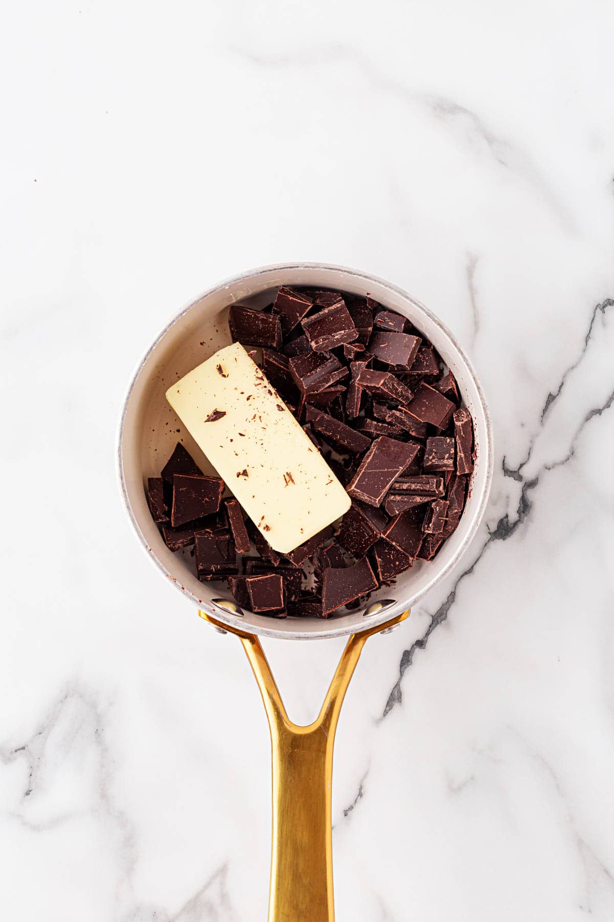 Chopped chocolate chunks and a stick of butter in a saucepan, ready to melt together