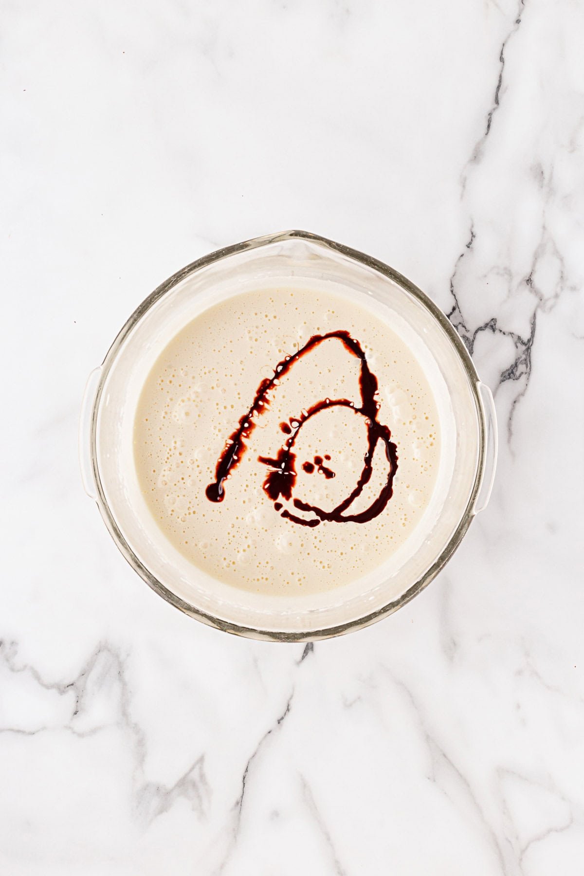 Whipped egg and sugar mixture in a glass bowl with vanilla extract swirled on top