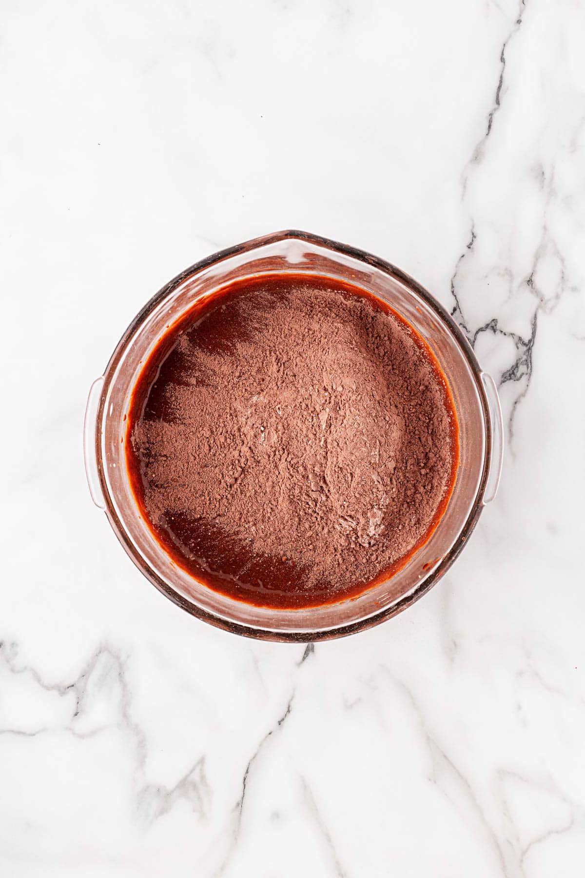 Cocoa powder added on top of chocolate batter in a mixing bowl before combining