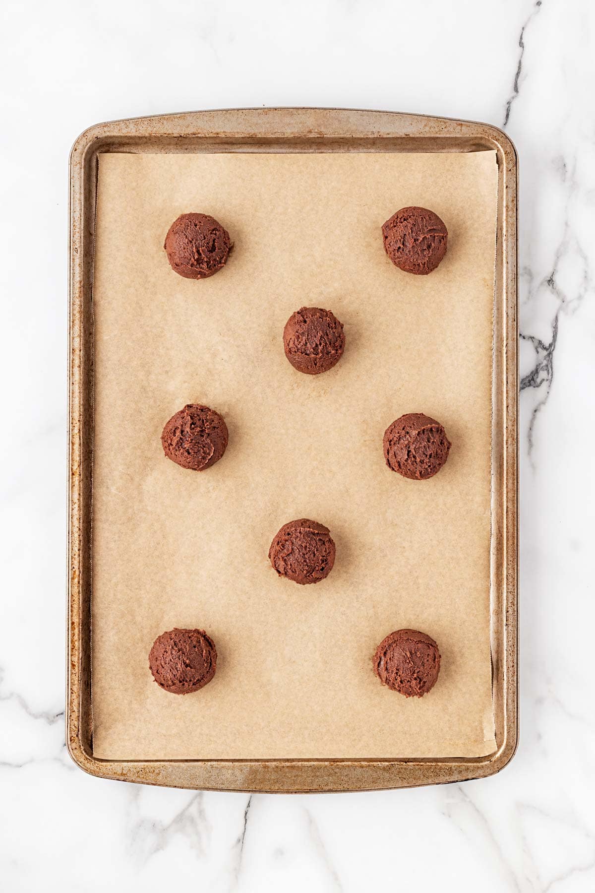 Scoops of chocolate cookie dough placed evenly on a parchment-lined baking sheet