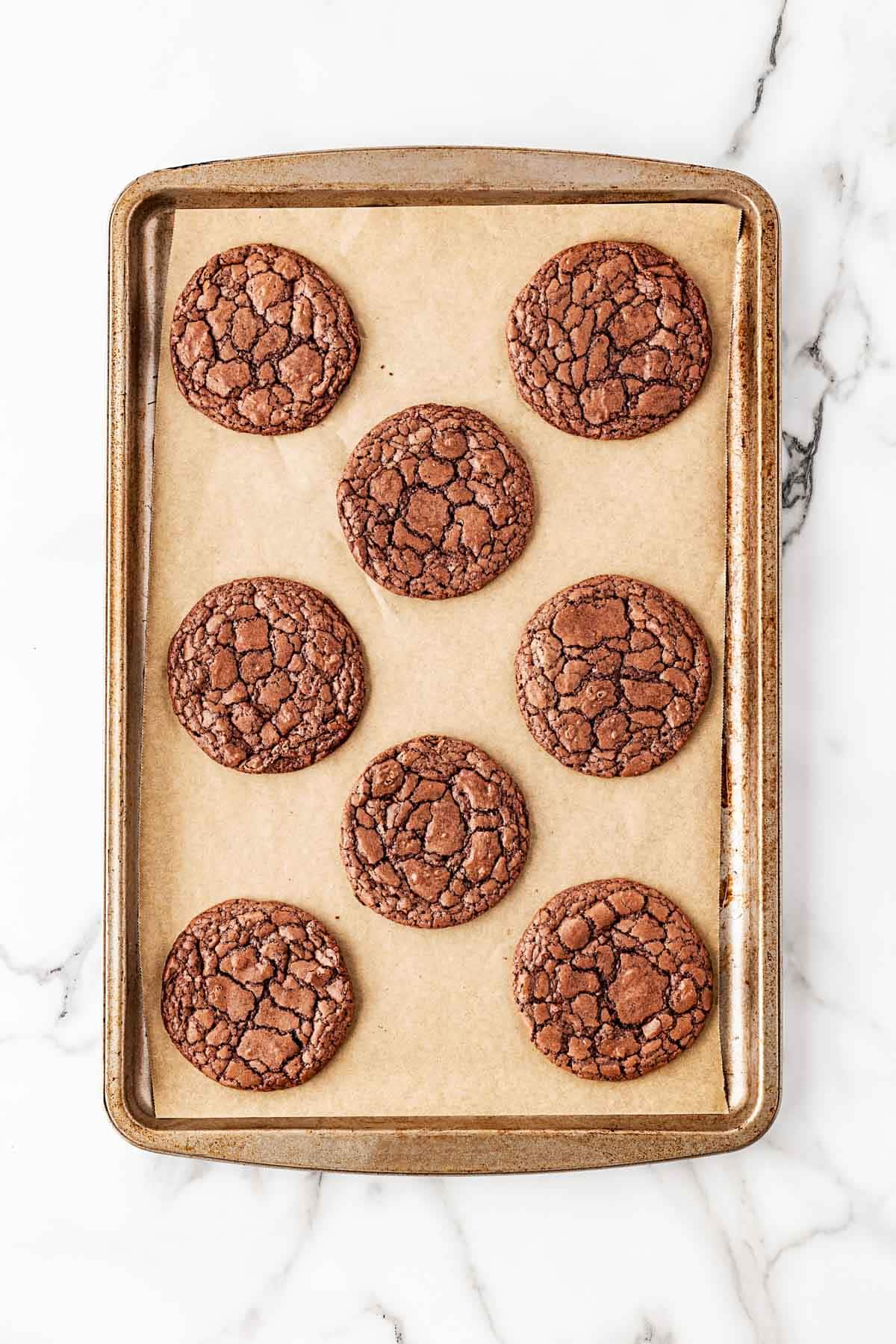 Freshly baked brownie cookies on a parchment-lined baking sheet with shiny crackled tops