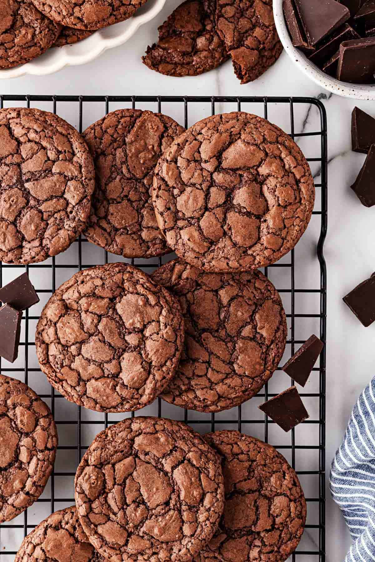Freshly baked brownie cookies cooling on a wire rack, surrounded by chocolate chunks