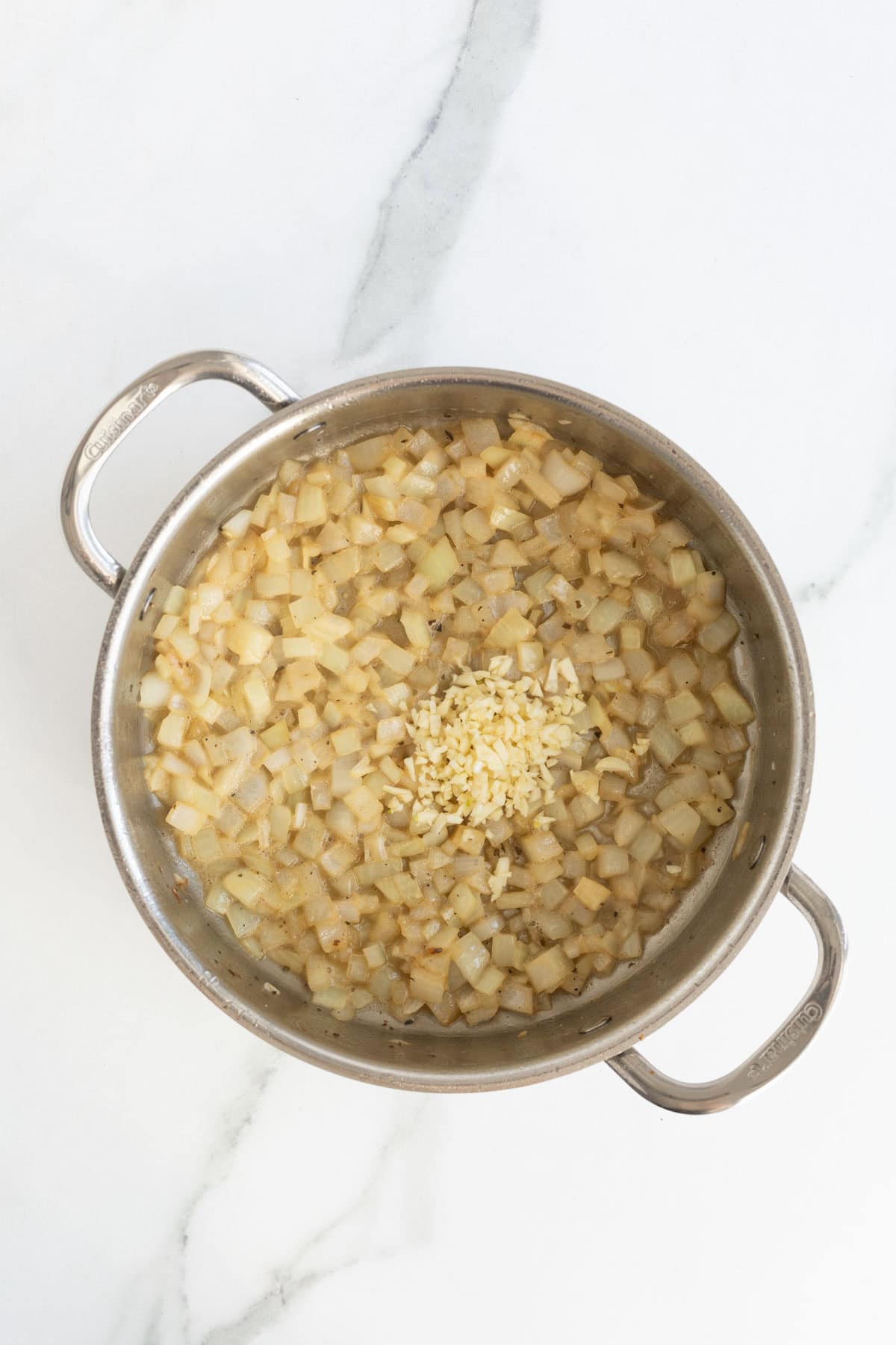 Chopped onions sautéing in a skillet with minced garlic added to the center