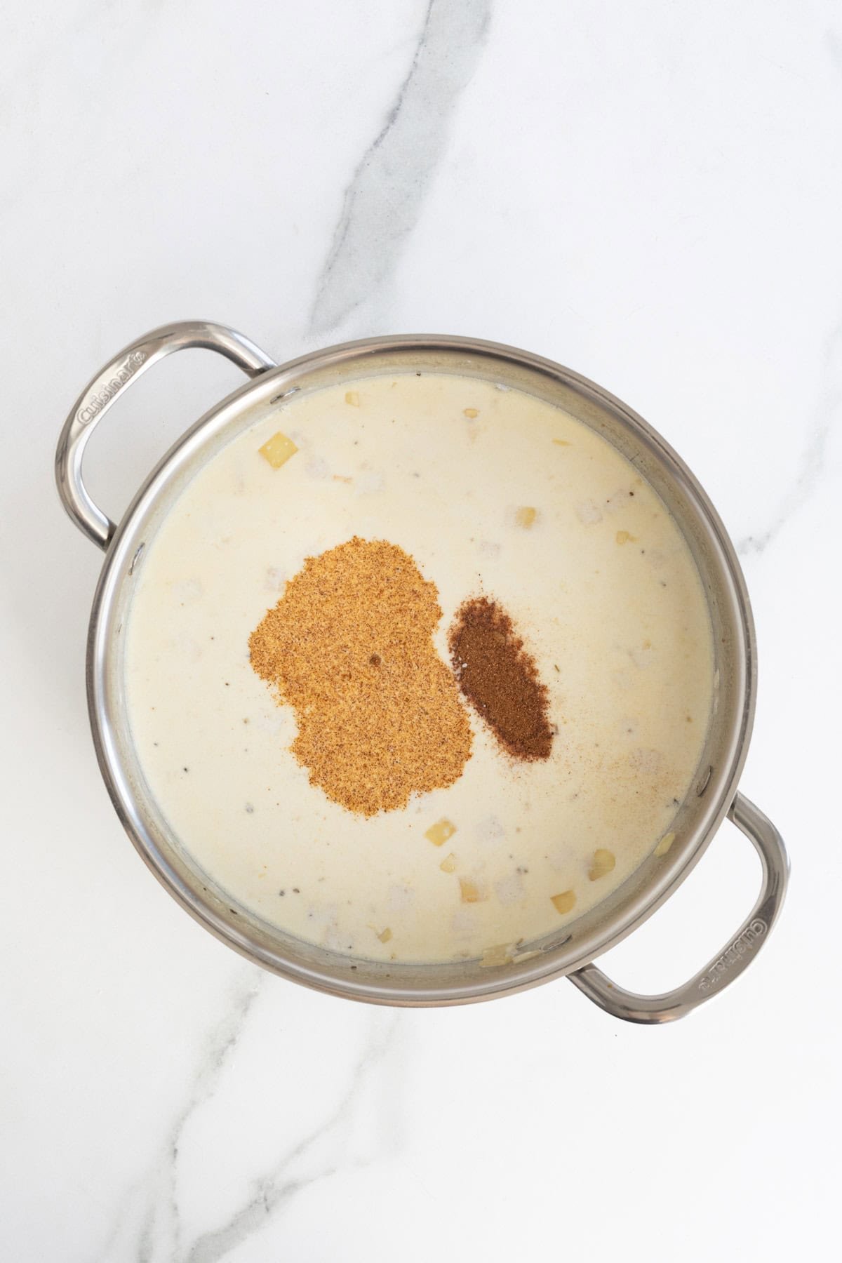 Alfredo sauce in a pot with spices added on top, ready to be mixed in