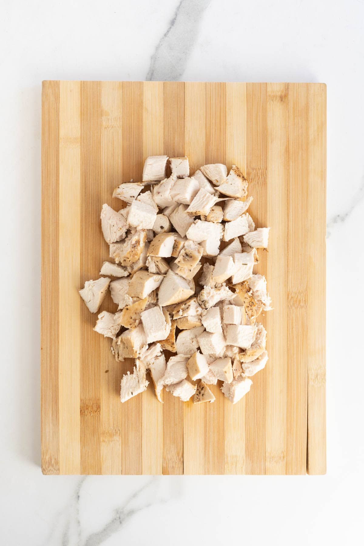 Cubes of cooked chicken breast piled on a wooden cutting board