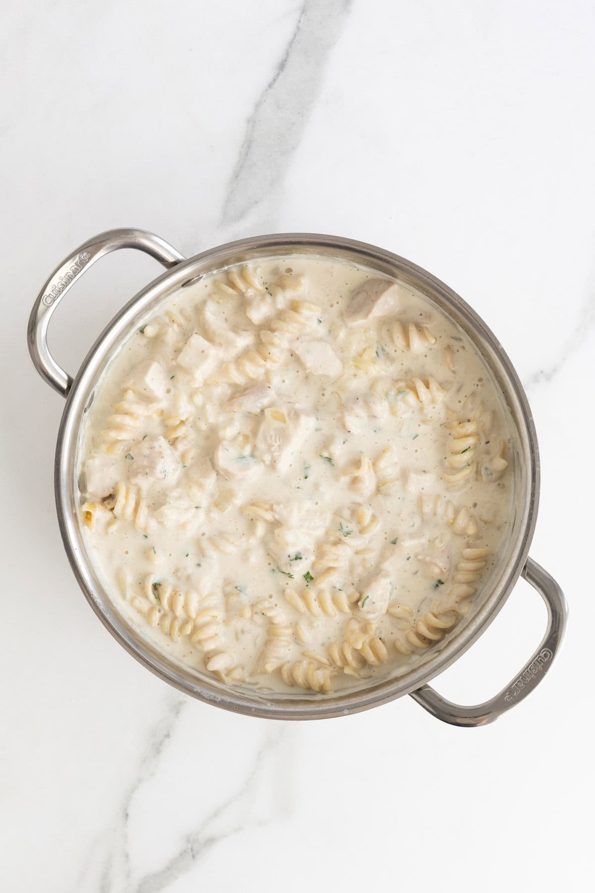 Cooked pasta and diced chicken coated in creamy alfredo sauce in a pot