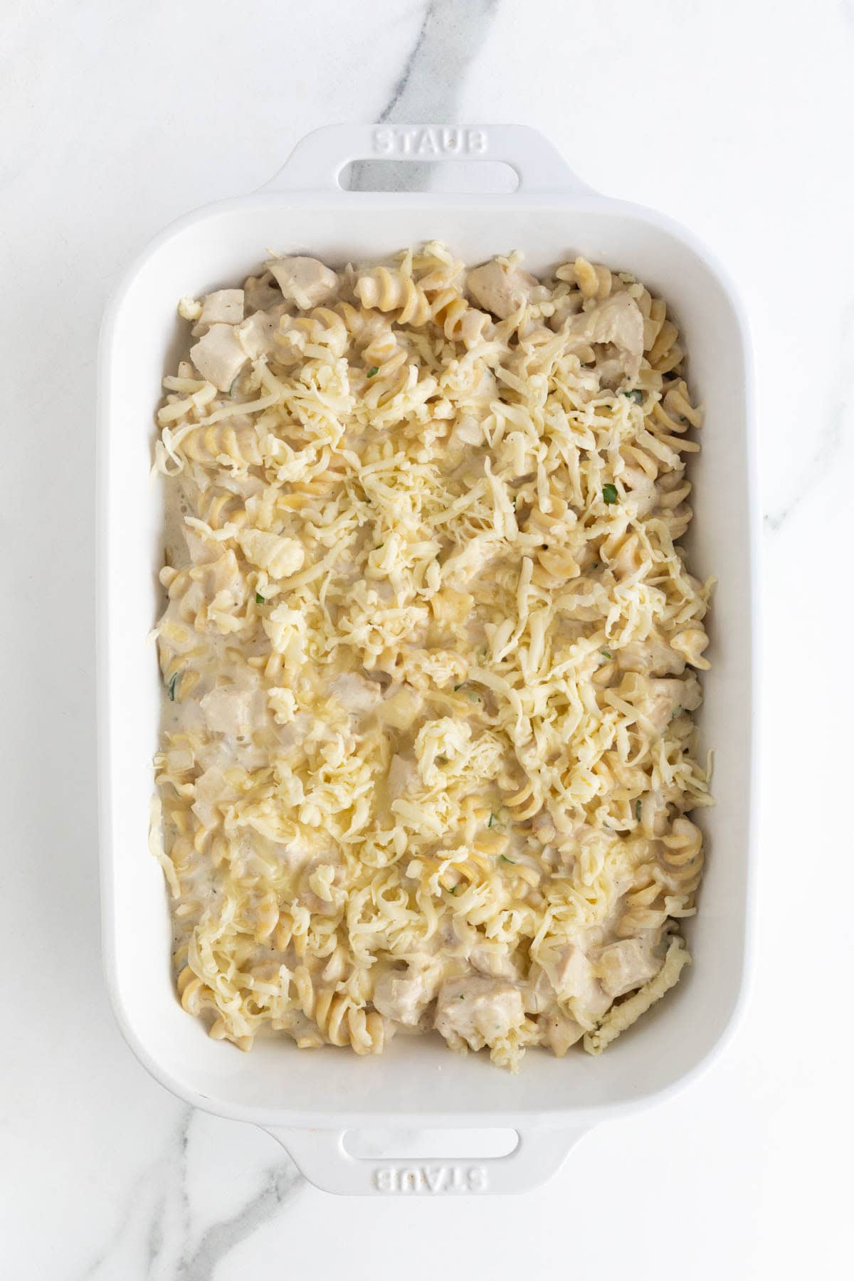 Unbaked chicken alfredo casserole in a white baking dish topped with shredded cheese