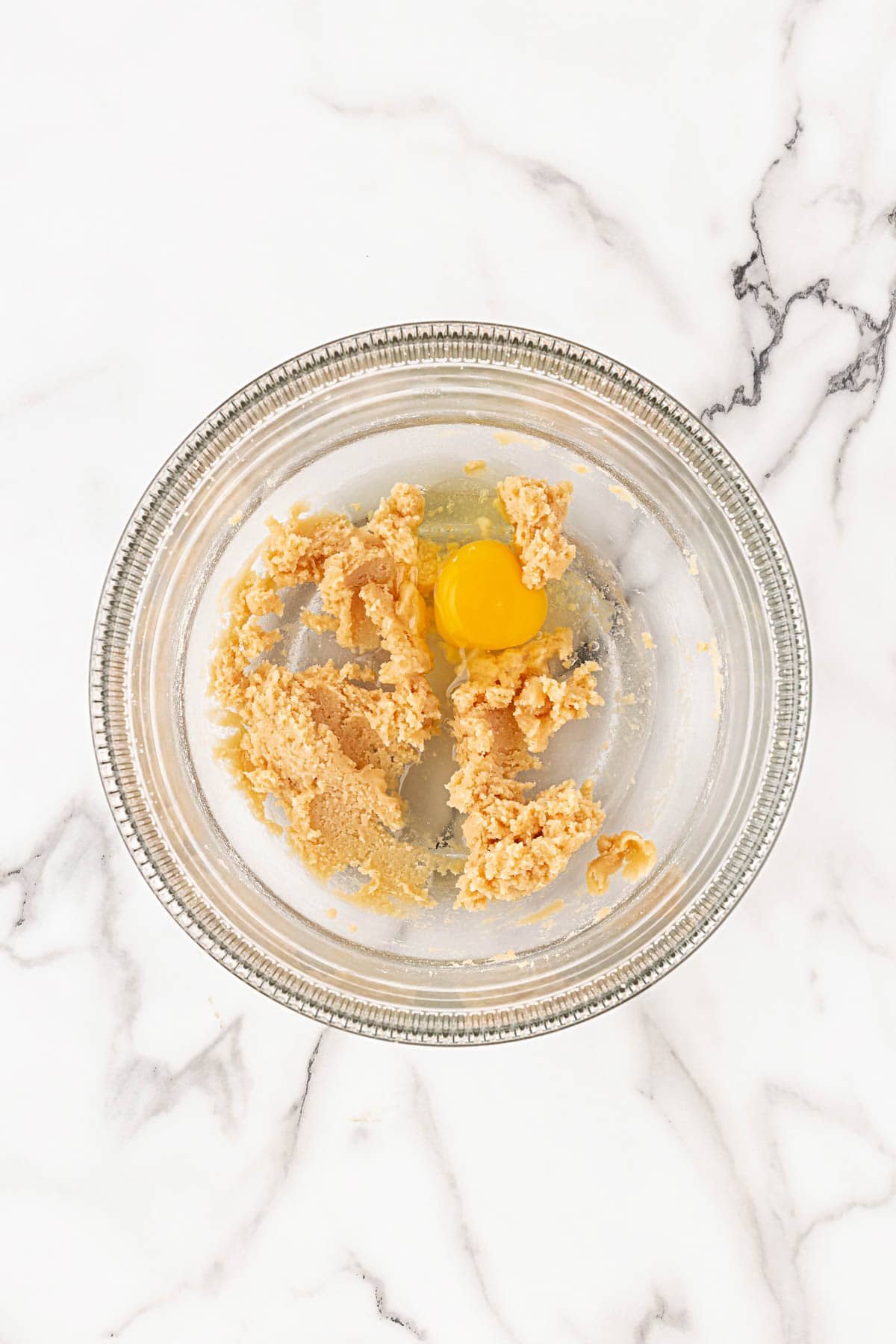 Mixing bowl with creamed butter and sugar mixture and a cracked egg on top