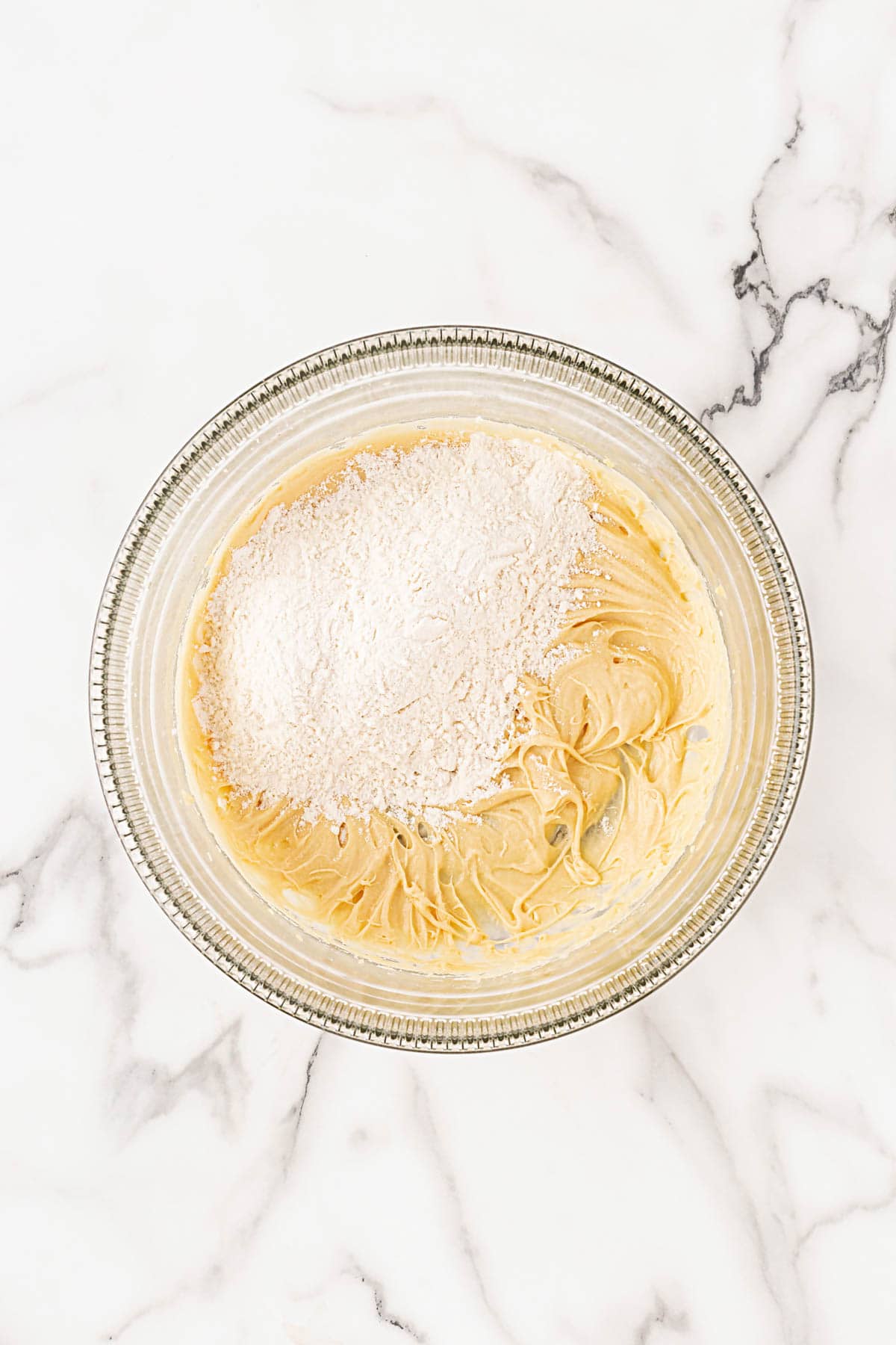 Mixing bowl with smooth, pale cookie dough topped with a mound of flour mixture before combining