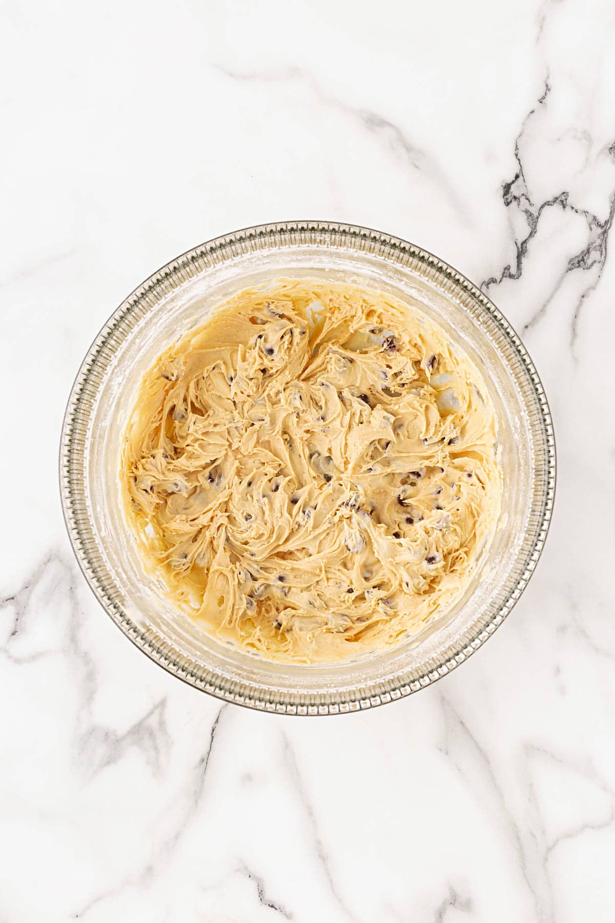 Fully mixed cookie dough in a glass bowl, speckled with chocolate chips
